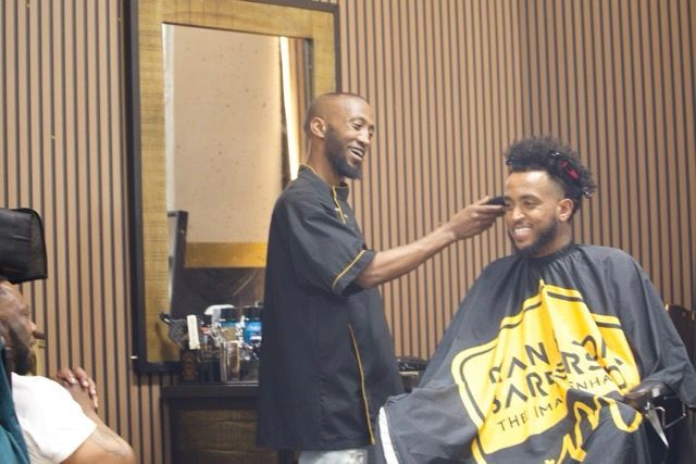 Barber giving a client a haircut in a shop. The client smiles.