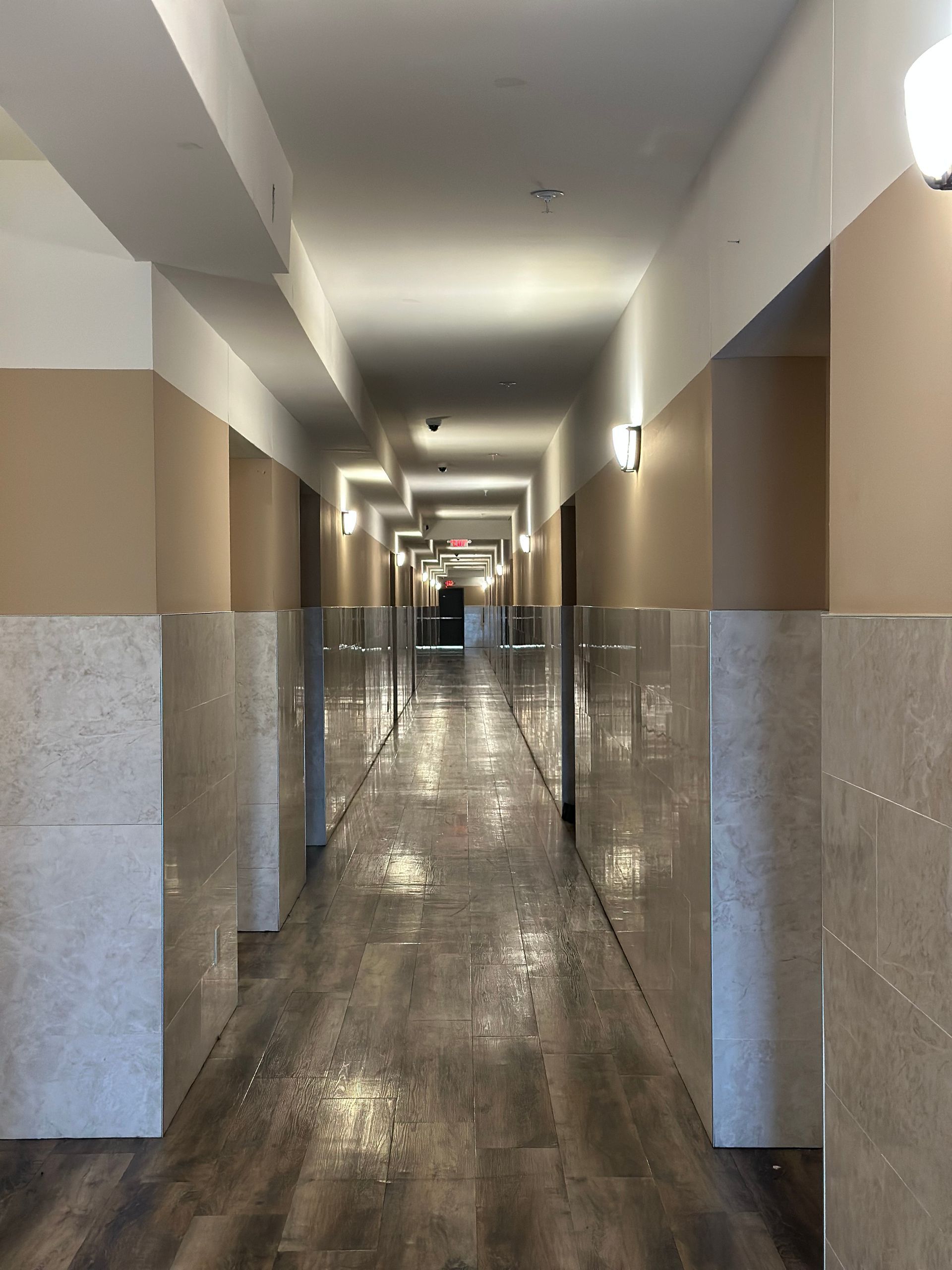 Long hallway with beige and white walls, tiled pillars, and wood-look flooring.