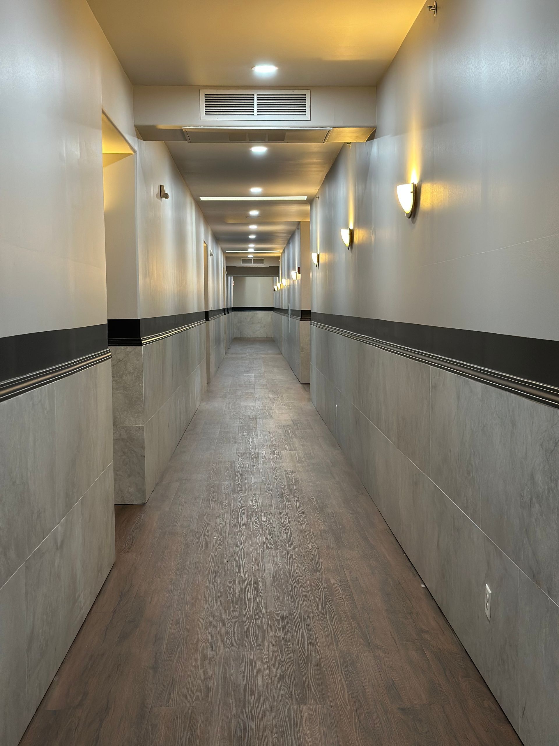 Long hallway with tile and wood flooring, sconce lighting.
