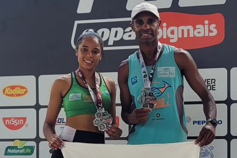 Dois medalhistas no pódio, segurando troféus diante do painel de fundo de um evento esportivo