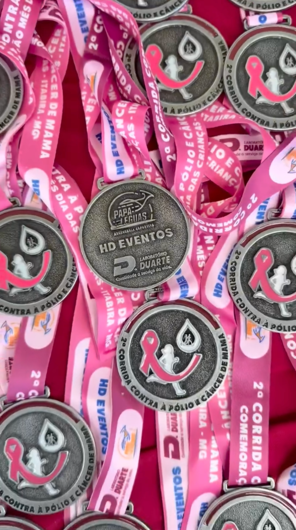 Fitas cor-de-rosa de conscientização e botões pretos redondos com logotipos brancos empilhados juntos.