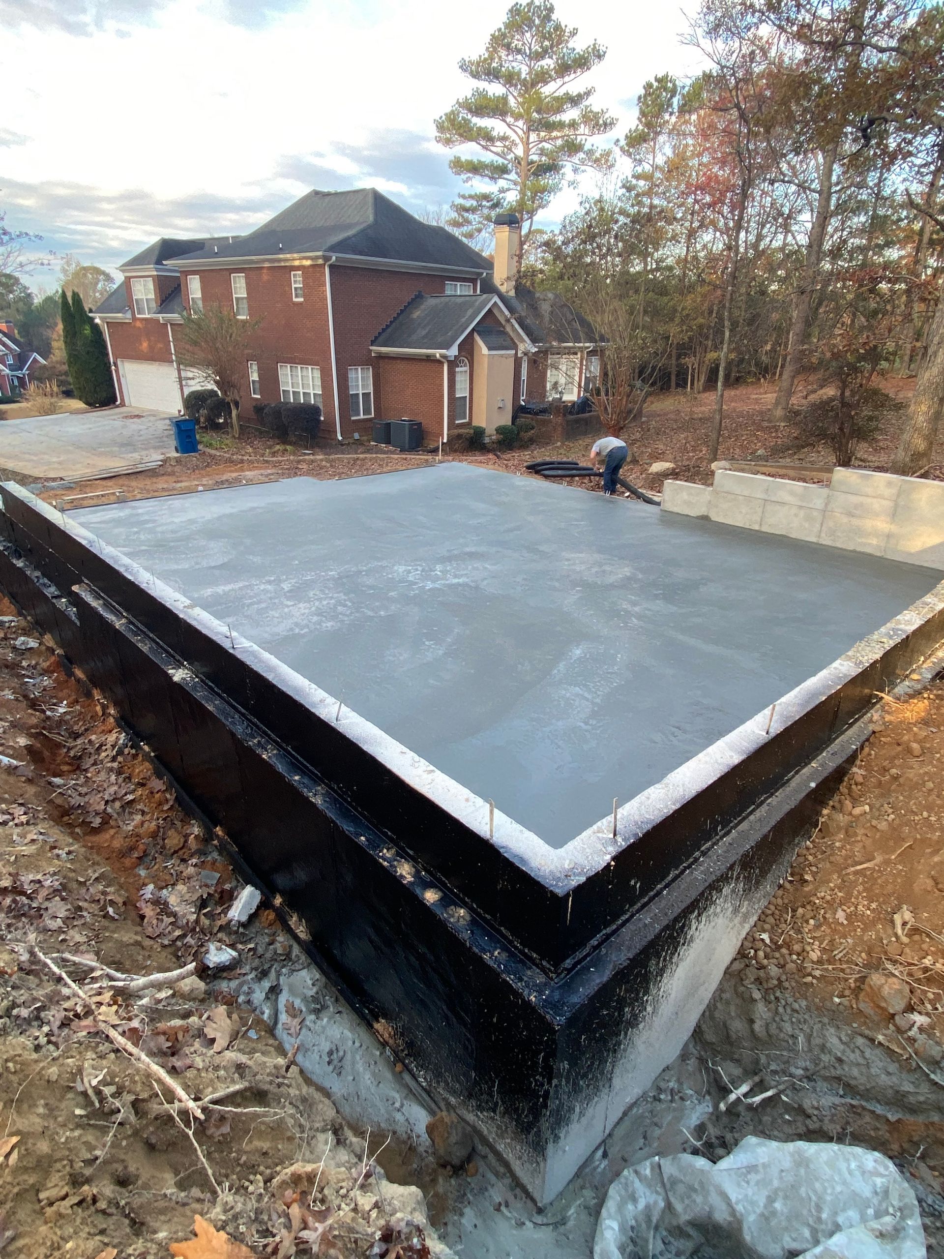 Newly poured concrete foundation next to a brick house. Person on the foundation.