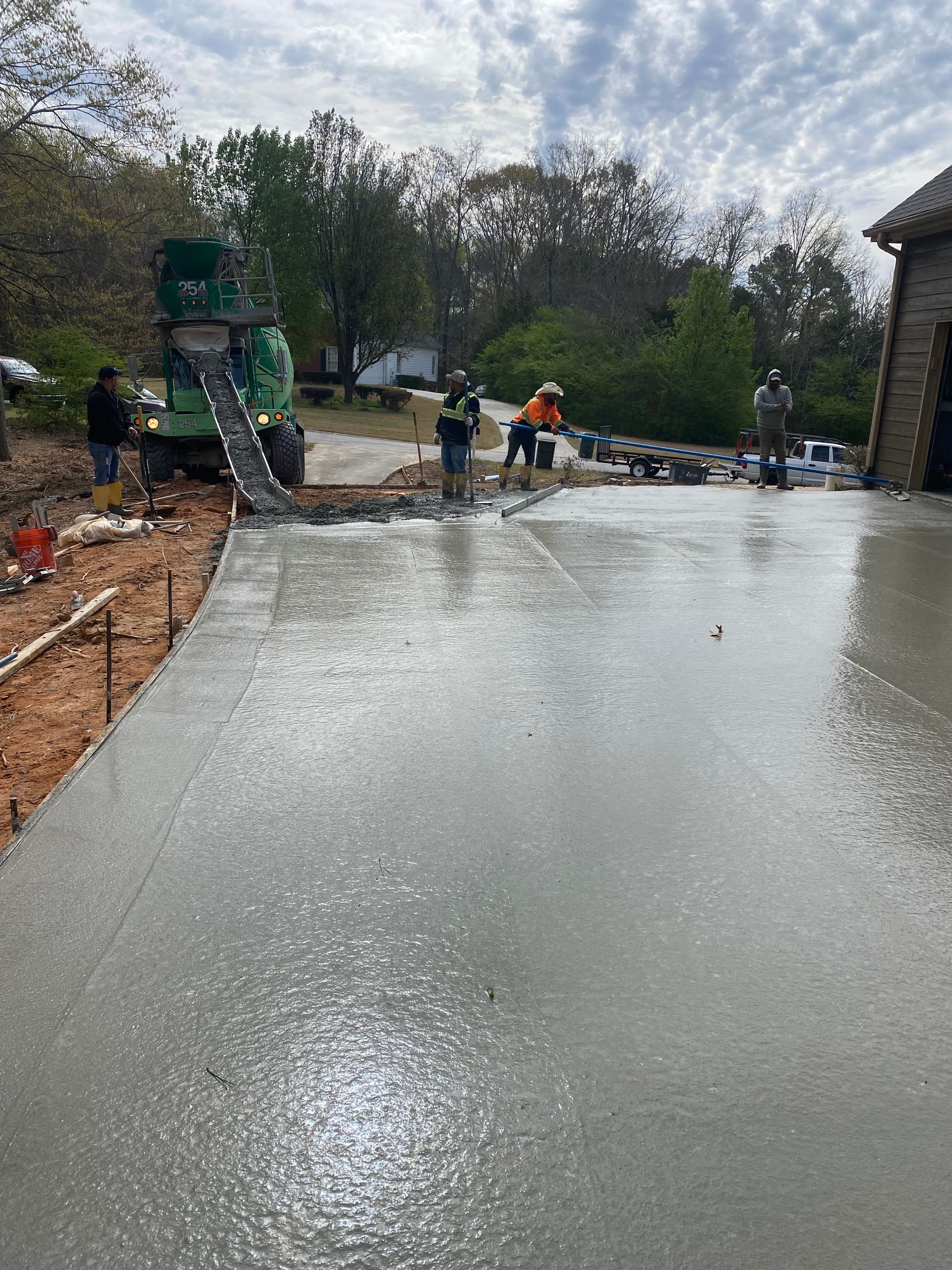 Construction workers pouring and smoothing wet concrete driveway on a sunny day.