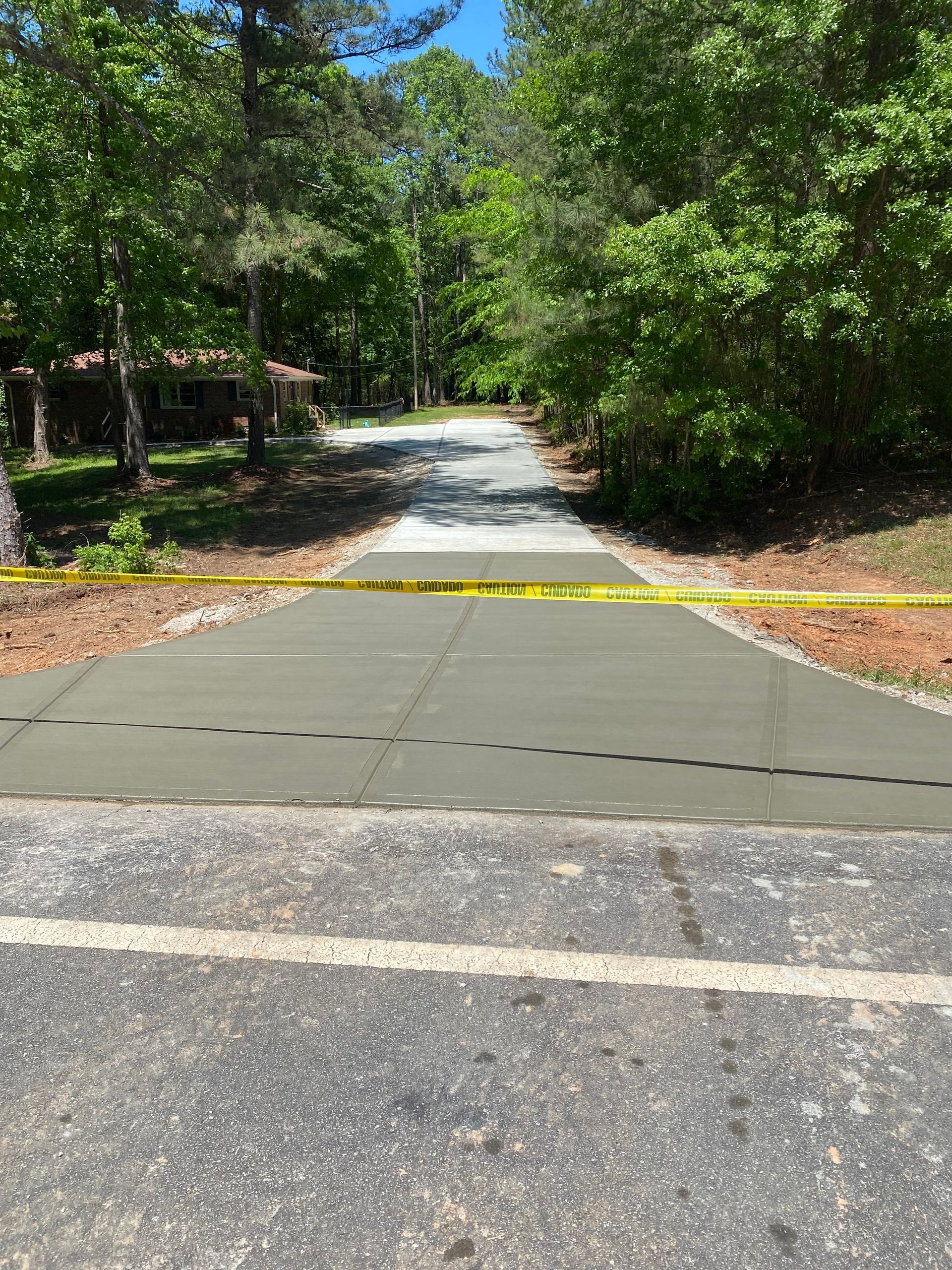 Paved road sectioned with darker asphalt and blocked by yellow caution tape, leading to a lighter gravel path.