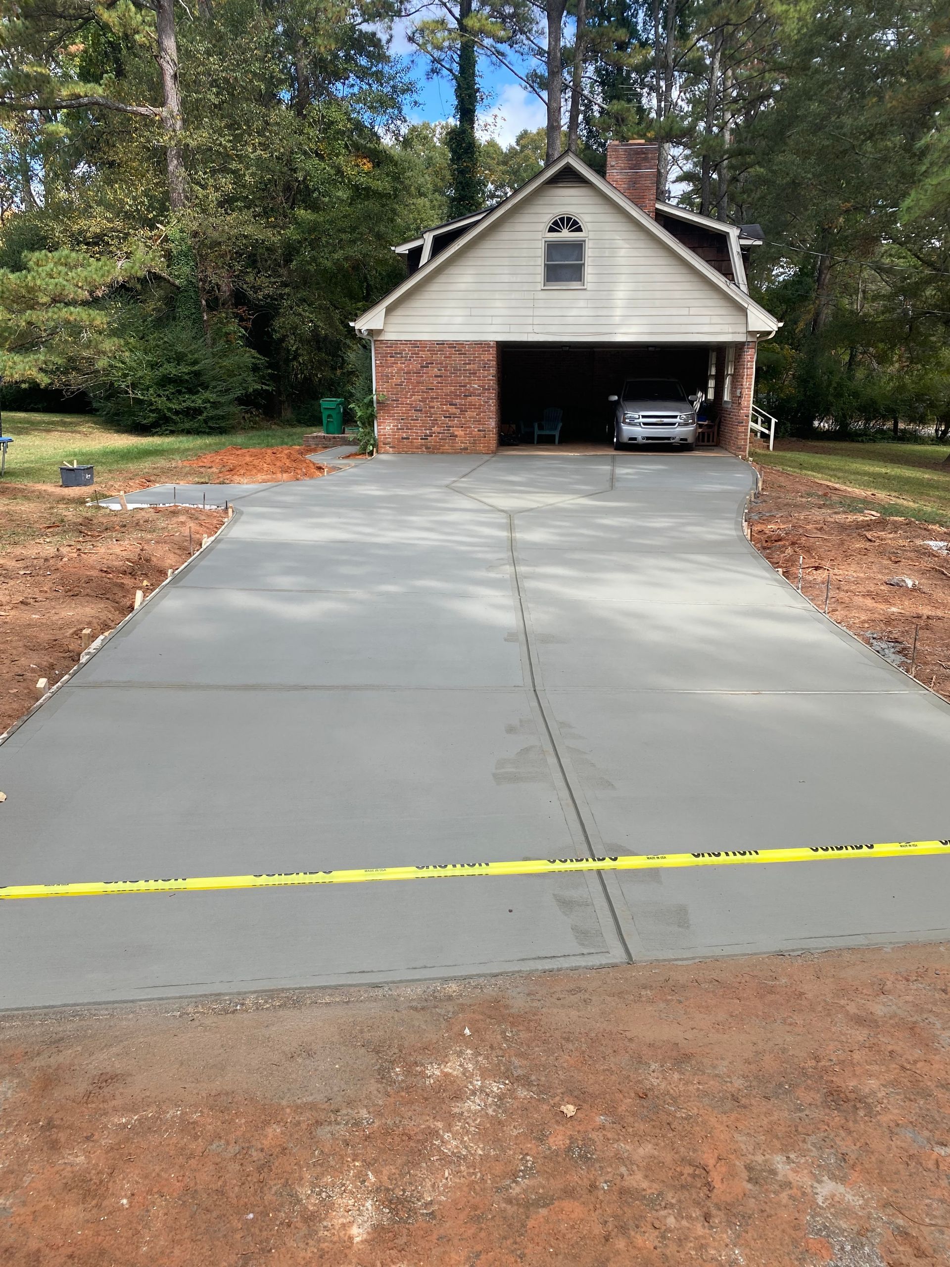 Newly poured concrete driveway leading to a house with a garage. Yellow caution tape across the front.