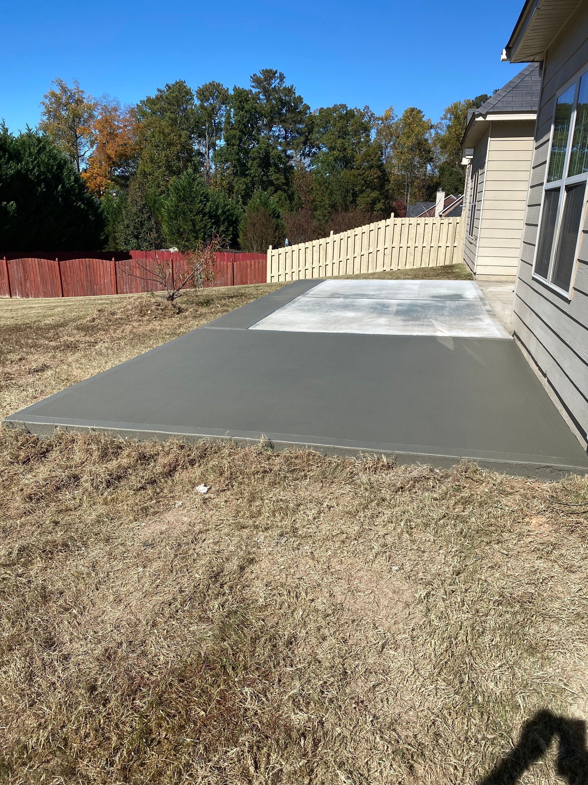 Newly poured concrete patio next to a house with a fence and trees in the background.
