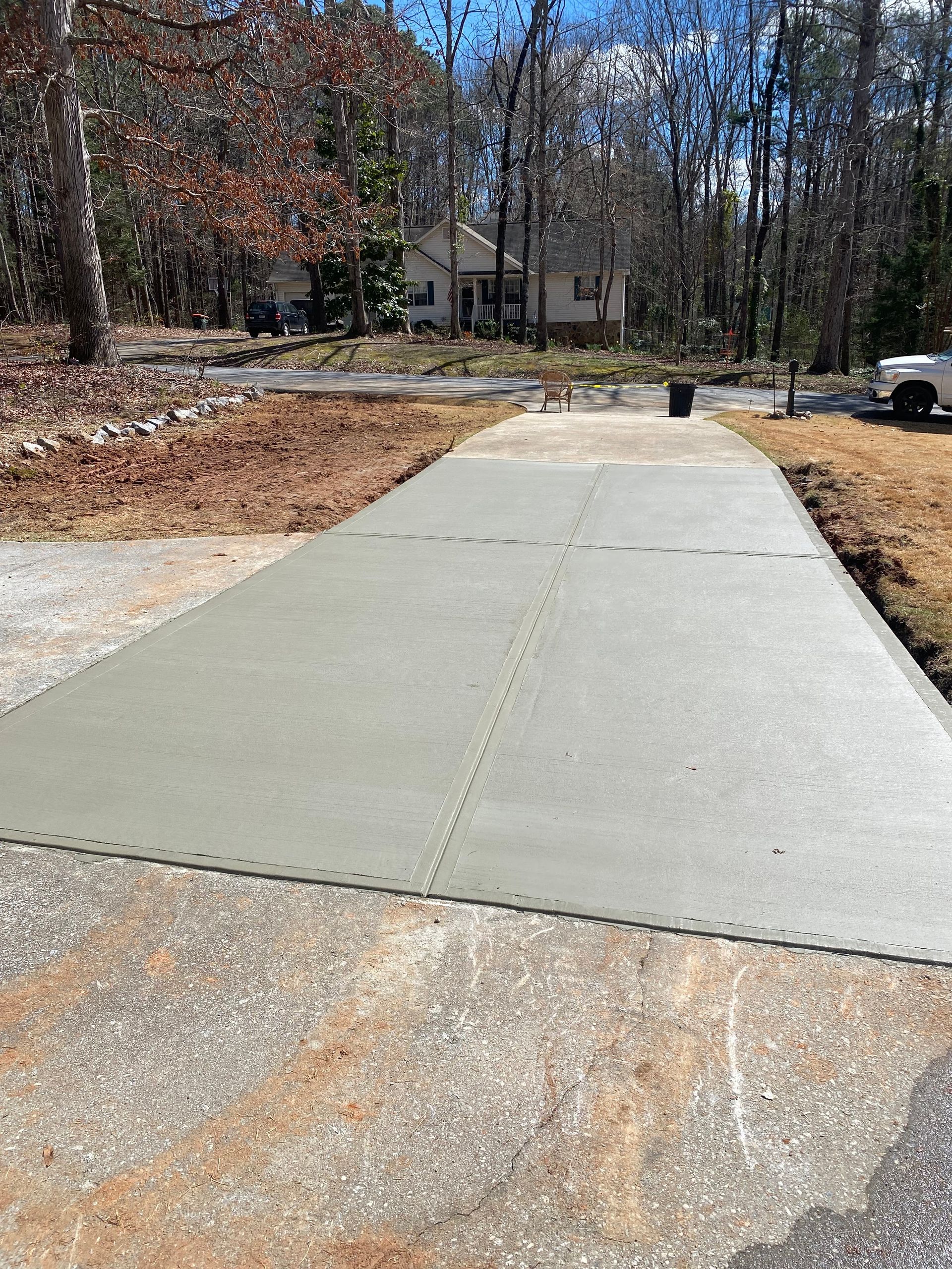 New concrete driveway section laid, light gray, next to older, worn concrete. House in background.