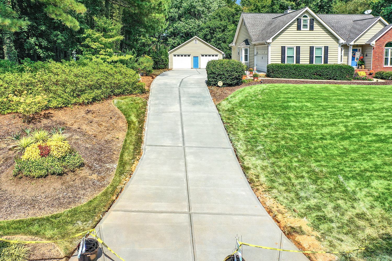 Concrete driveway leading to house with detached garage; lush green lawn and landscaping on both sides.