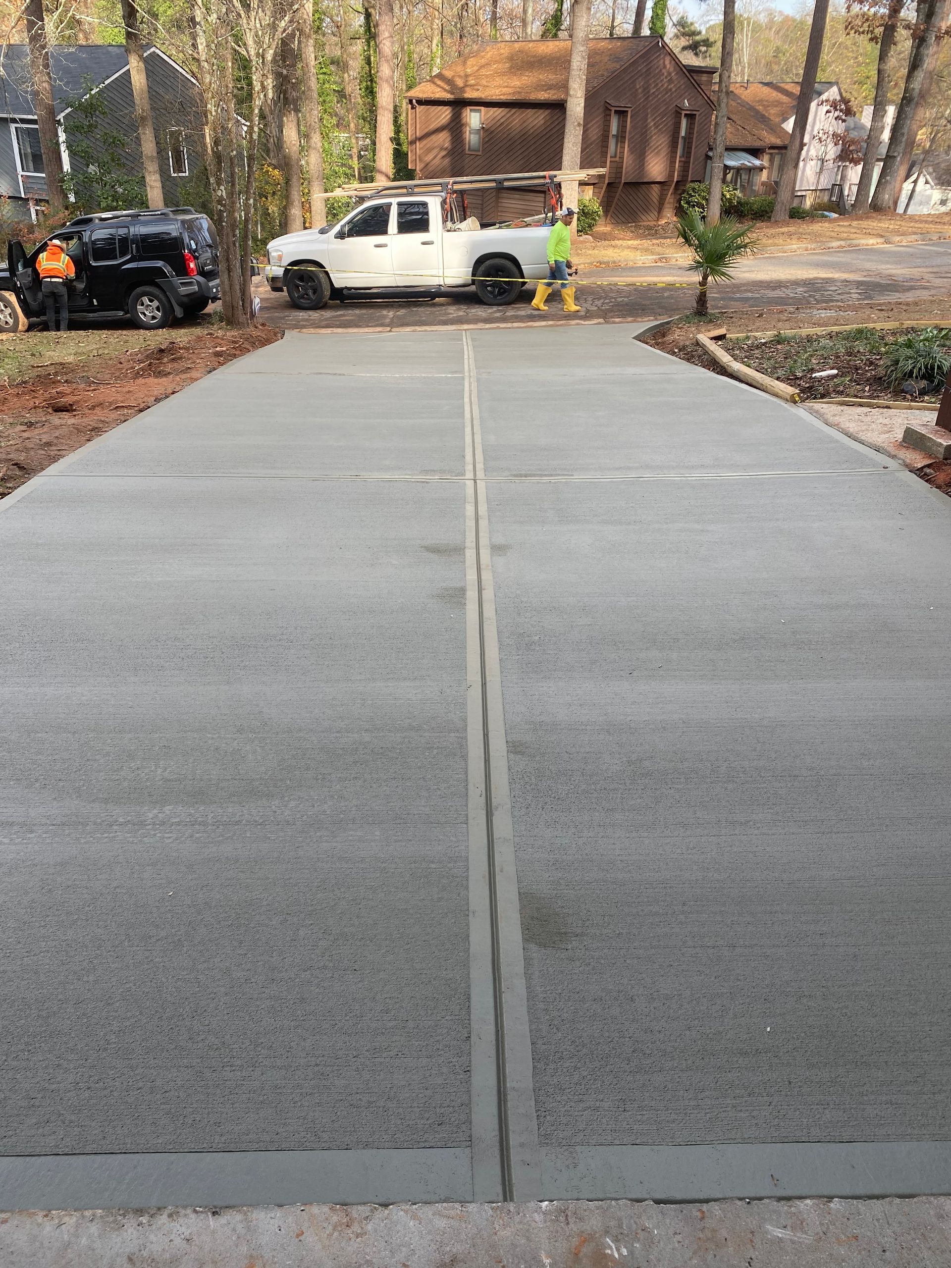 Newly poured concrete driveway with expansion joints; a white truck and two people are visible in the background.