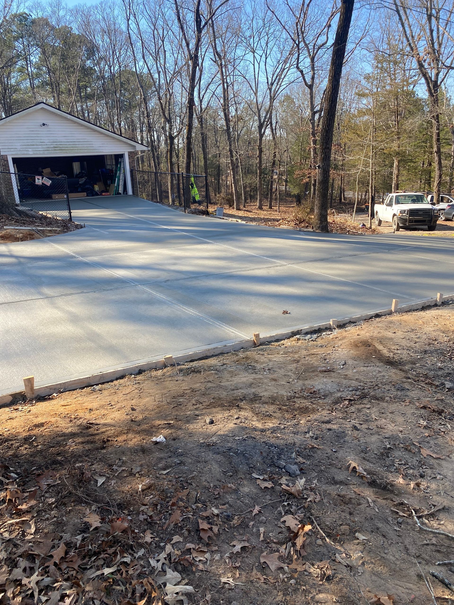 New concrete driveway being installed near a garage in a wooded area.