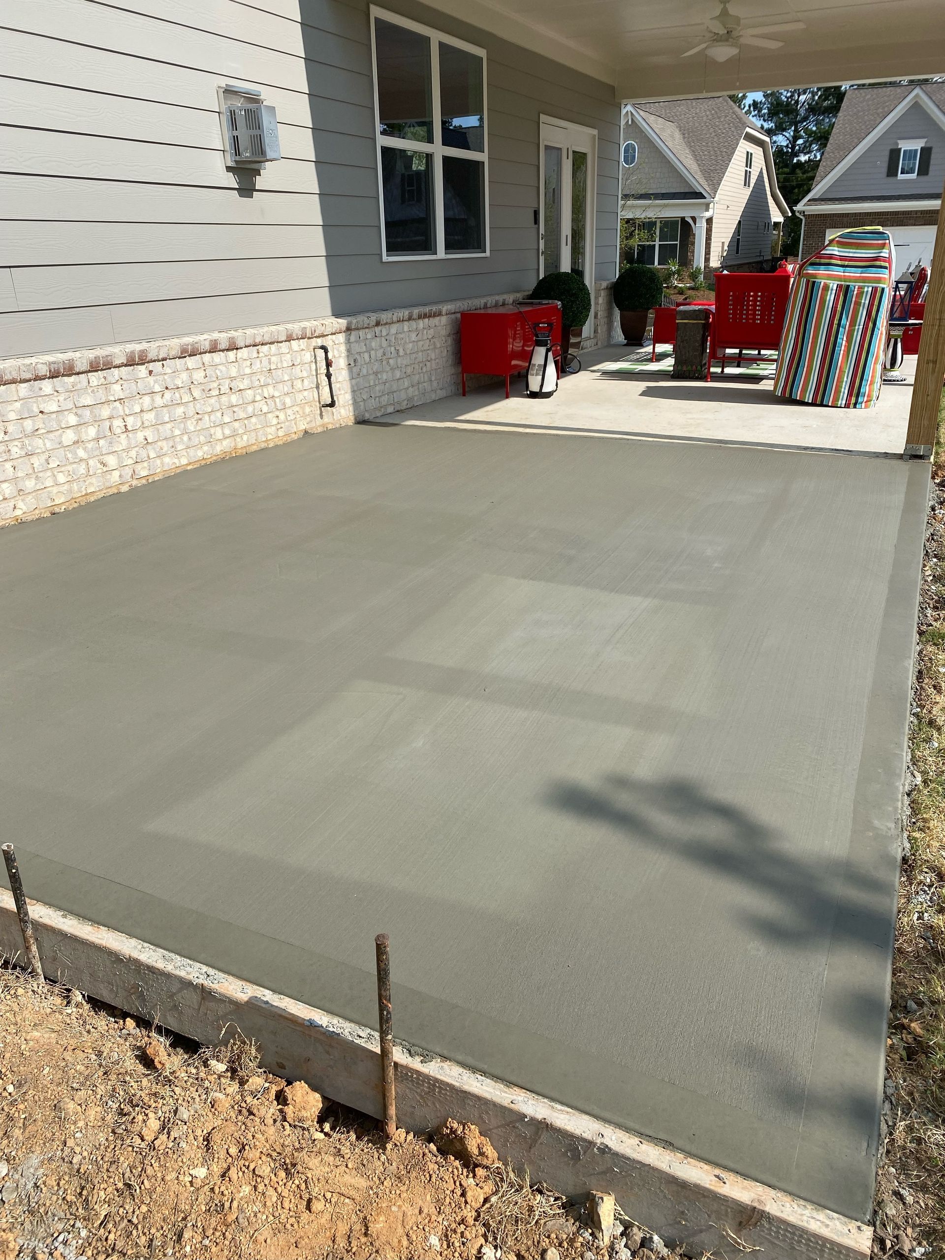 Newly poured concrete patio next to a house with exposed aggregate foundation and part of a covered porch.