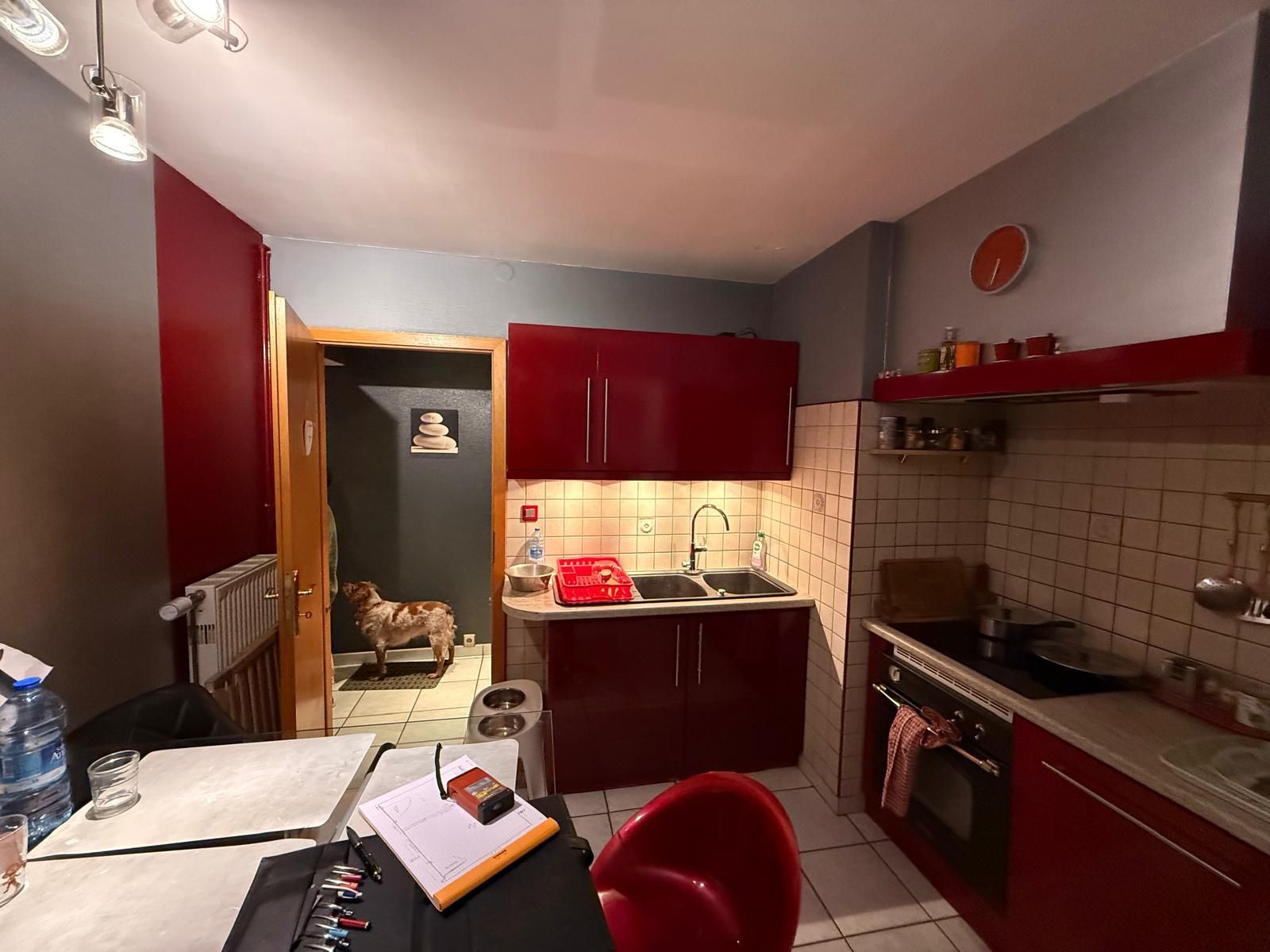 Cuisine compacte avec placards rouges, crédence en carrelage blanc et table au premier plan