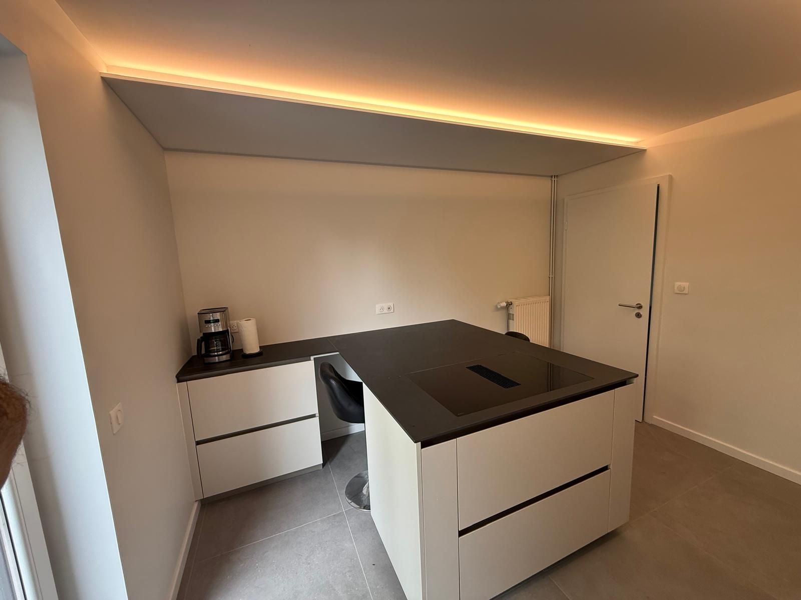 Cuisine moderne et minimaliste avec armoires blanches, comptoirs noirs et éclairage encastré au plafond