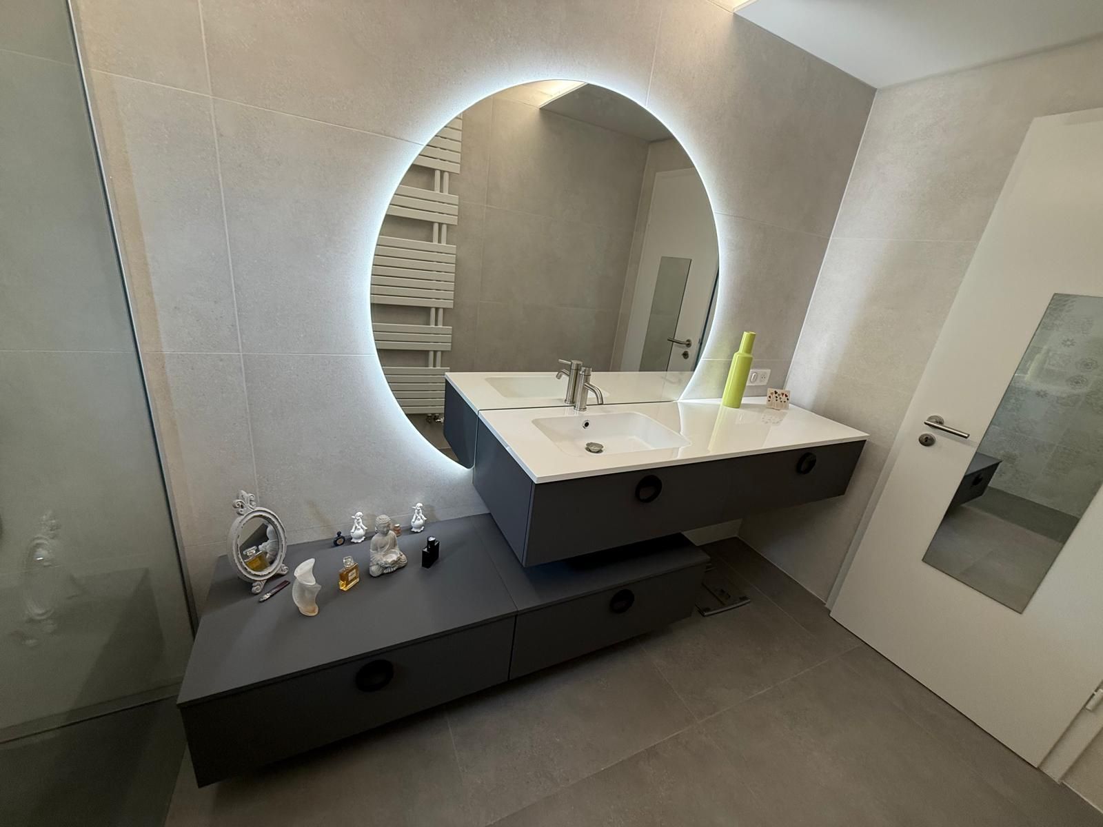 Meuble-lavabo moderne avec miroir rond, lavabo blanc, tiroirs noirs et murs carrelés