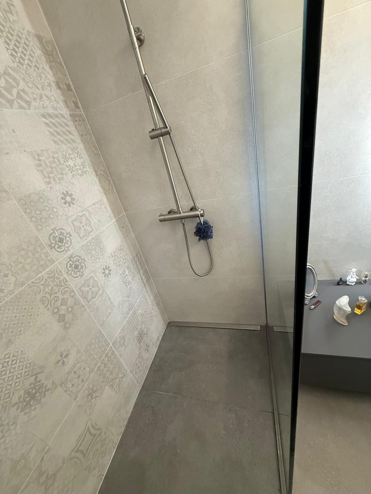 Cabine de douche avec pommeau et flexible chromés à côté d'un lavabo dans une salle de bain carrelée