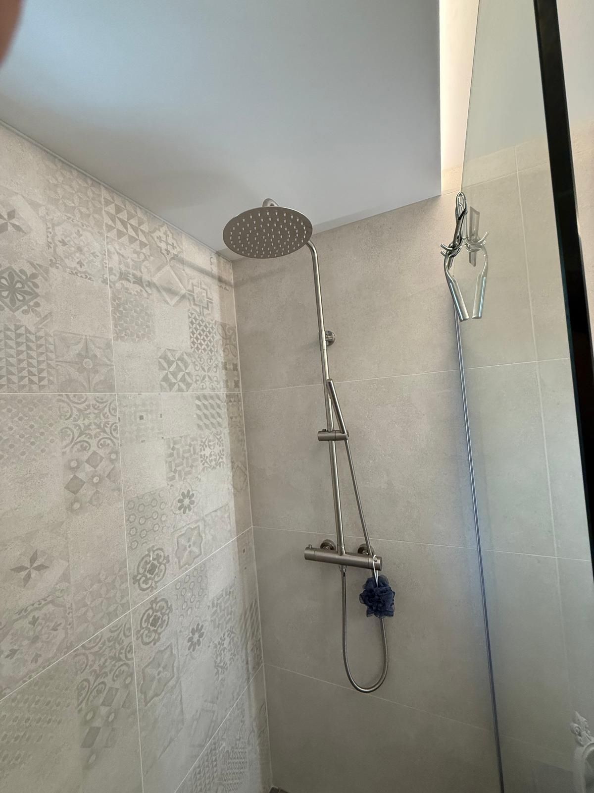 Petite salle de bain avec douche, murs carrelés à motifs, pommeau de douche effet pluie et douchette murale.