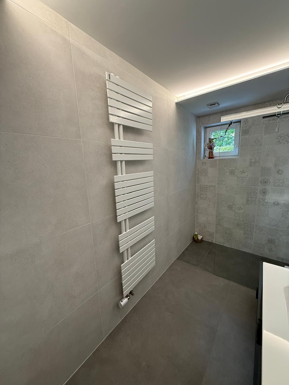 Salle de bains moderne avec murs carrelés gris, sèche-serviettes mural blanc et petite fenêtre.