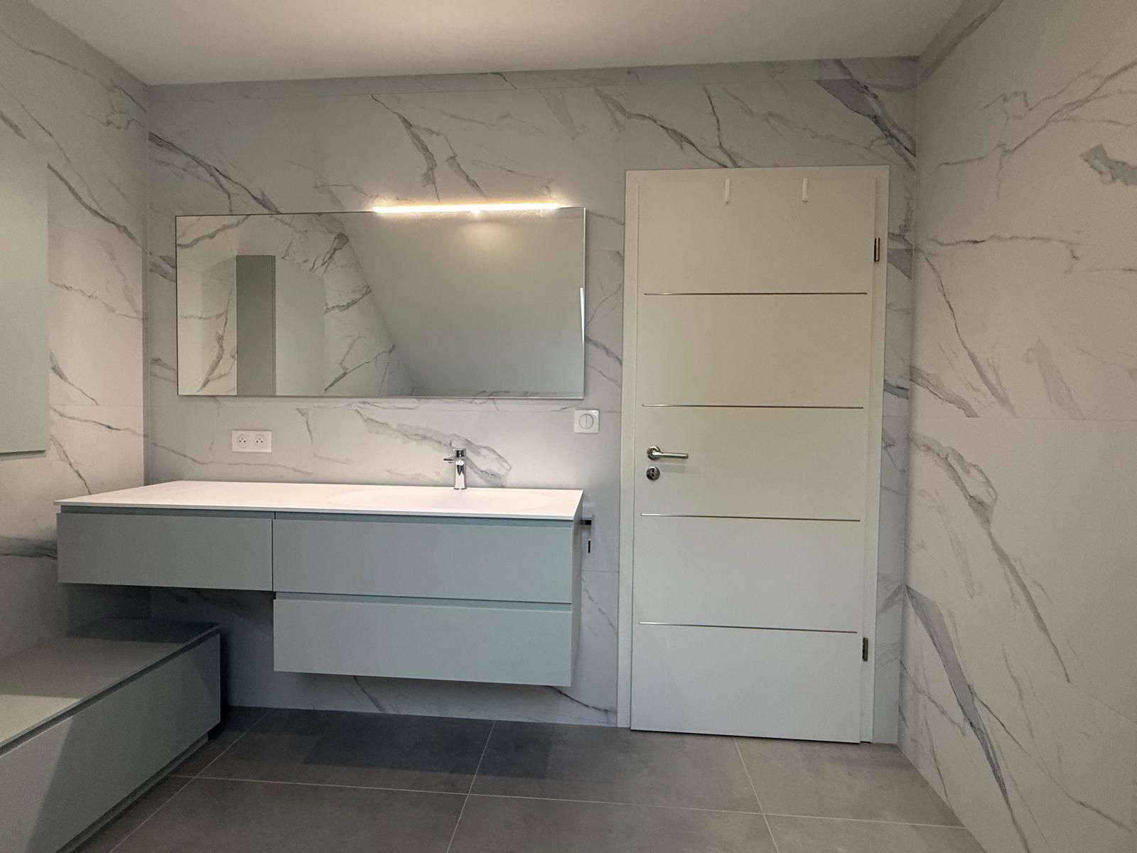 Salle de bains moderne avec murs imitation marbre, meuble-lavabo suspendu, miroir et porte blanche