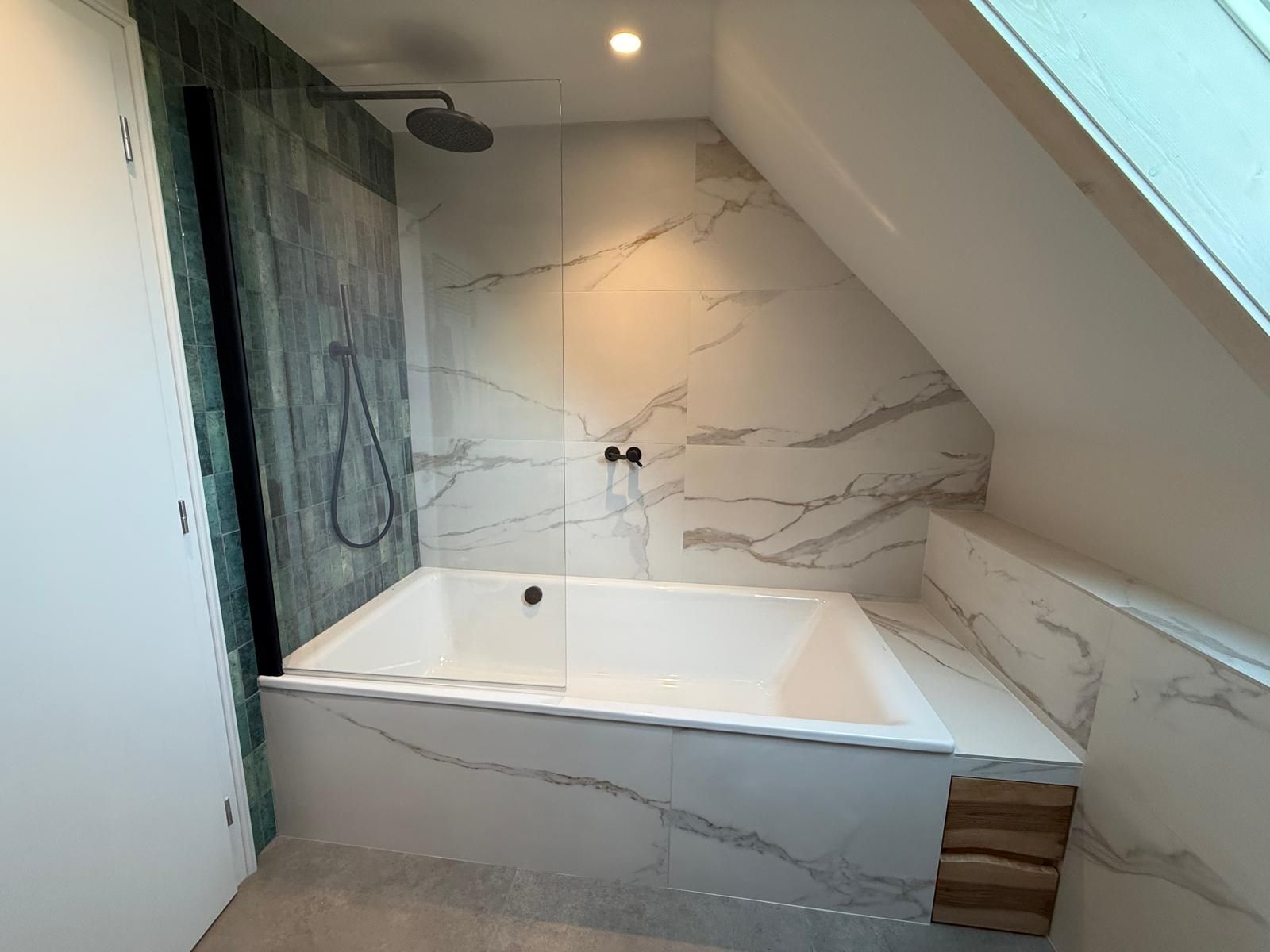 Salle de bains moderne avec baignoire blanche, murs en marbre, paroi de douche foncée et plafond en pente.