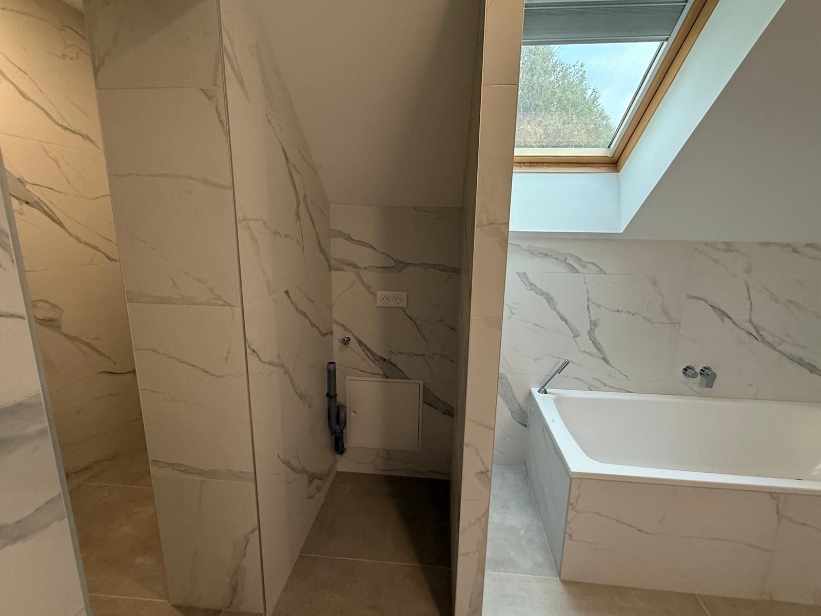 Salle de bains moderne avec grands carreaux de marbre blanc, baignoire et fenêtre de toit.