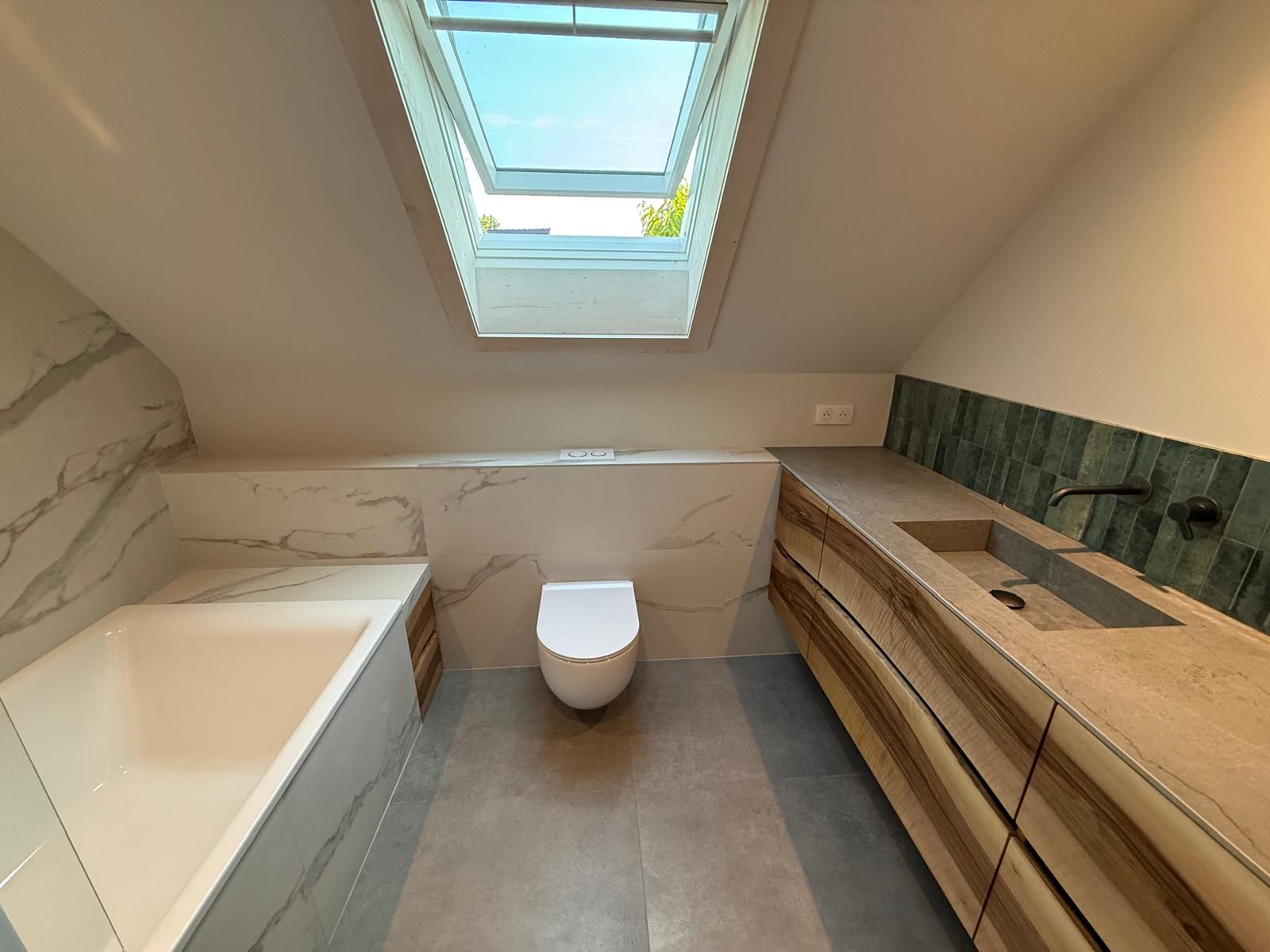 Salle de bains moderne avec puits de lumière, baignoire blanche, toilettes suspendues et meuble-lavabo en bois avec lavabo.