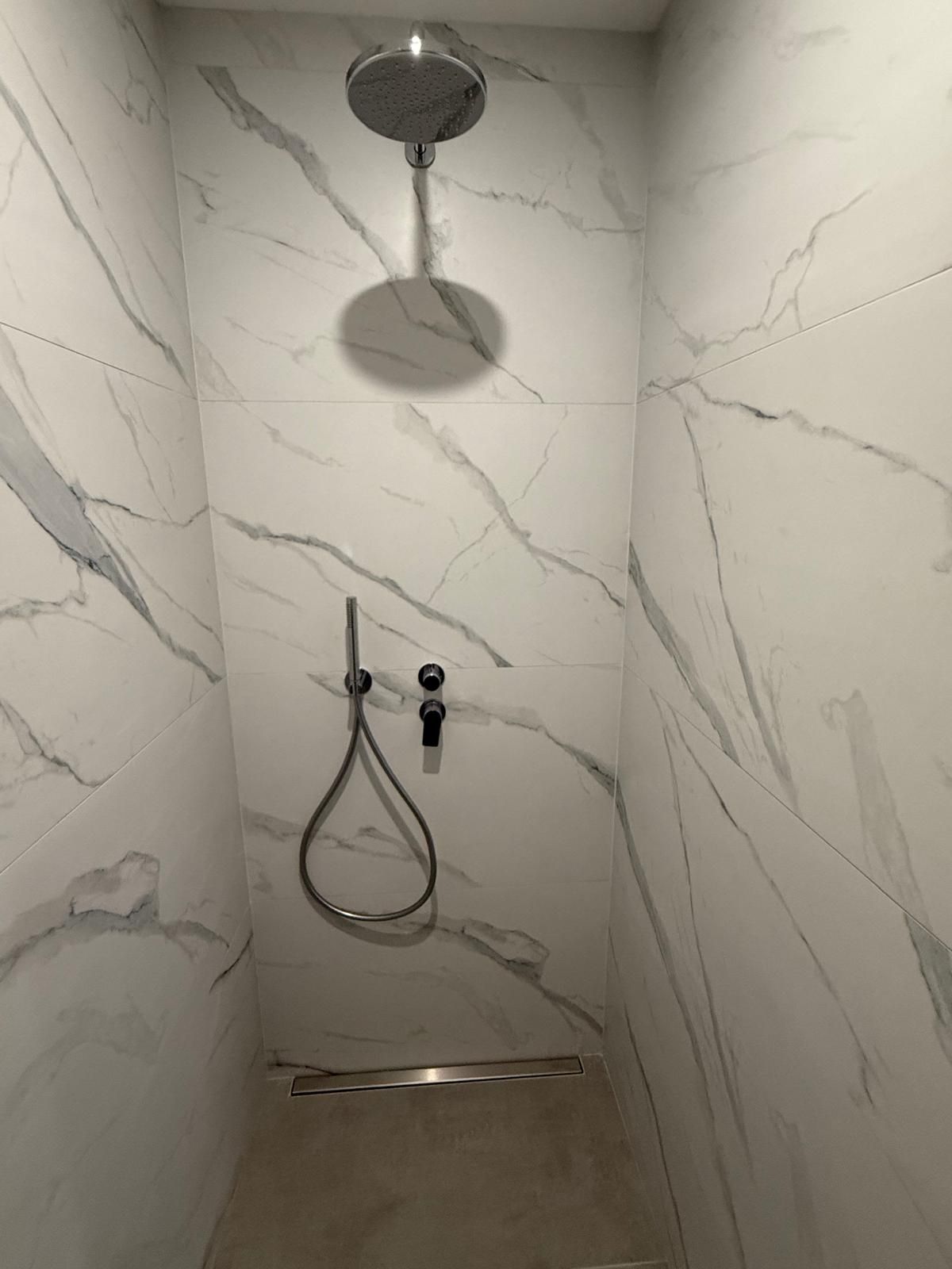 Cabine de douche carrelée en marbre avec pommeau de douche mural et douchette.