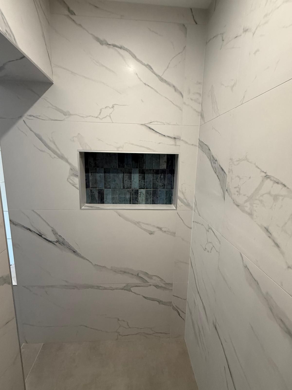Cabine de douche carrelée en marbre avec une ouverture de fenêtre encastrée et un insert en mosaïque foncée