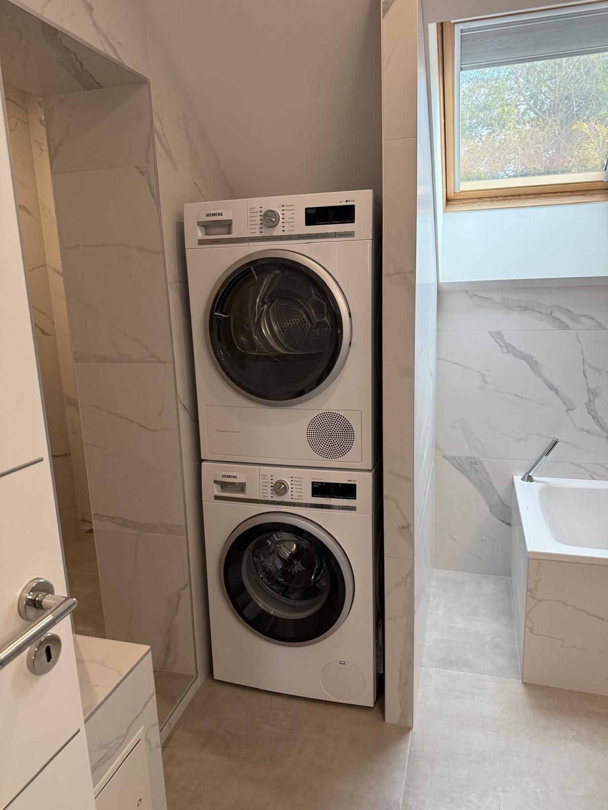 Laveuse et sécheuse superposées dans un coin étroit de la salle de bain, à côté de la douche et du lavabo.