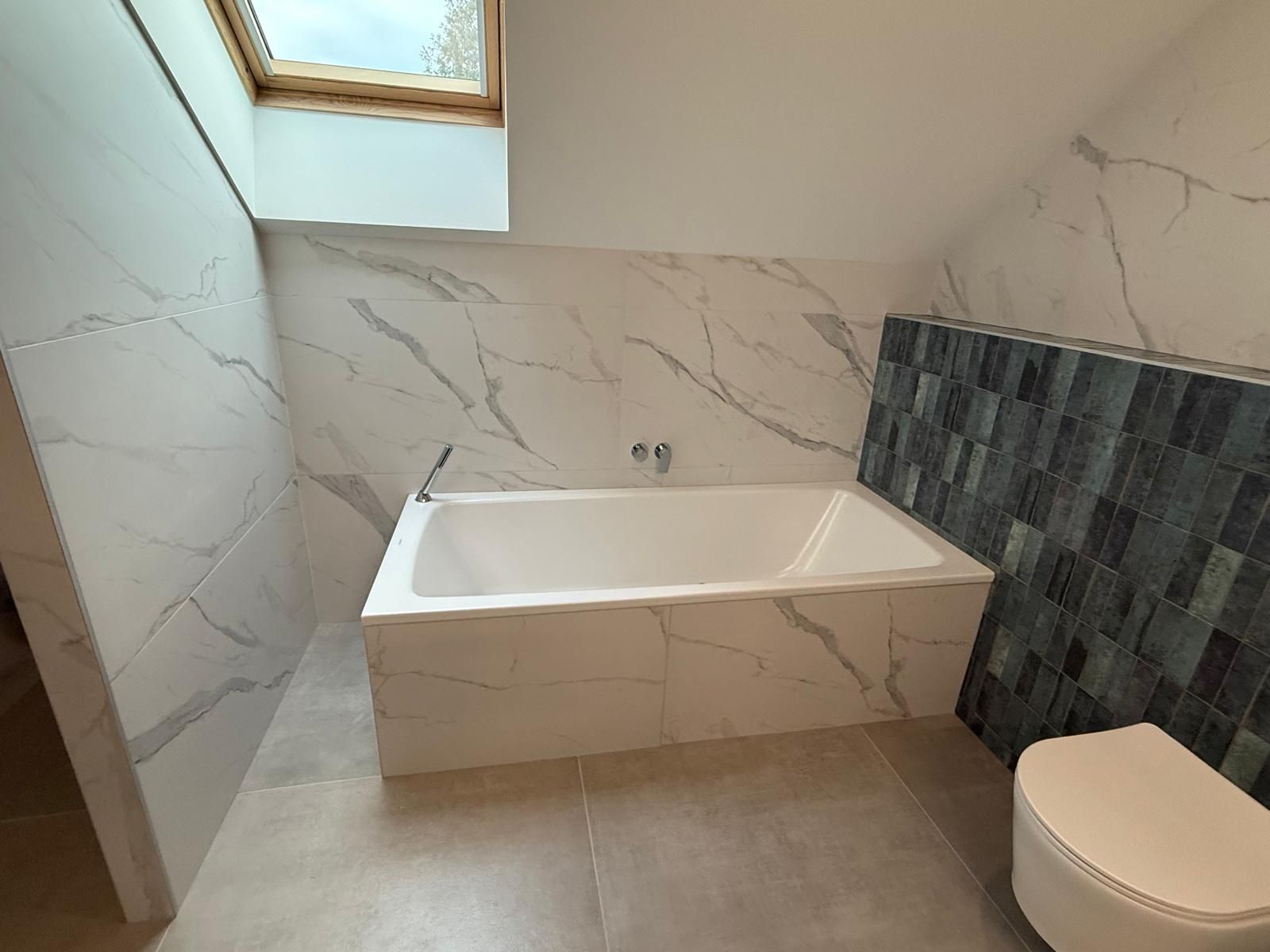 Salle de bains moderne avec baignoire blanche, murs carrelés en marbre et un mur d'accent en mosaïque à côté des toilettes.