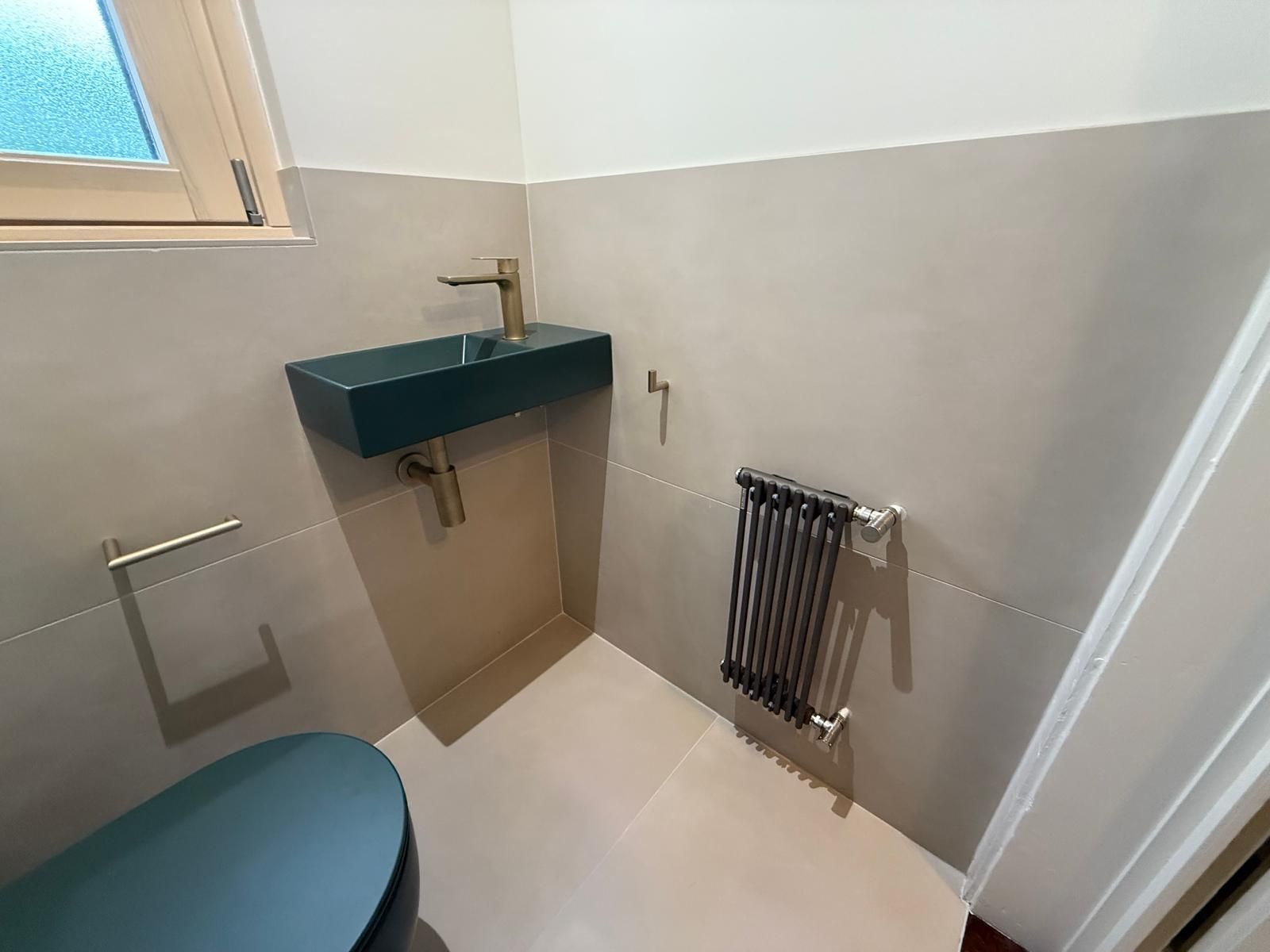 Petite salle de bains avec toilettes, lavabo, porte-serviettes et radiateur dans une pièce gris clair
