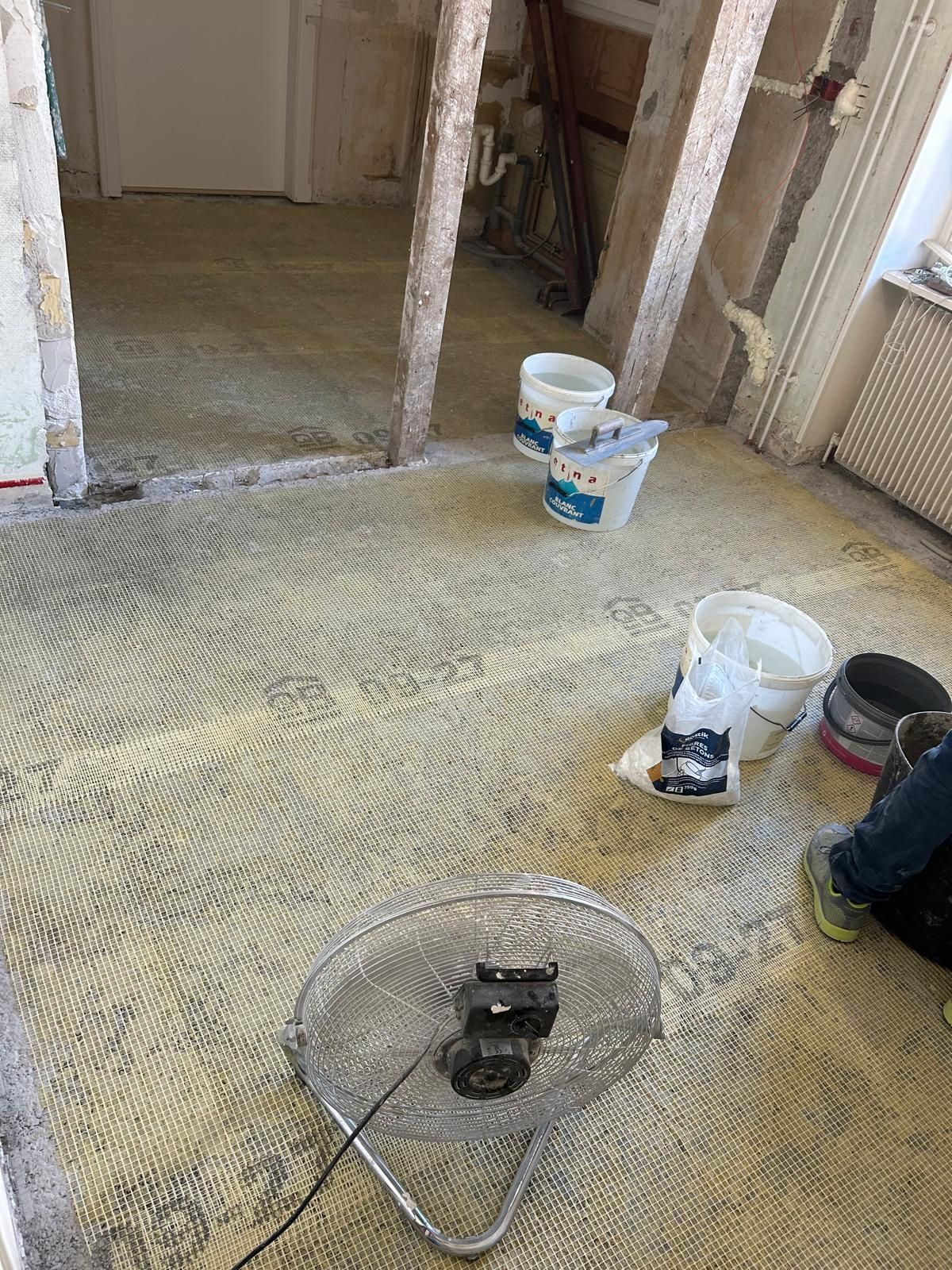 Pièce en rénovation avec moquette arrachée, seaux de peinture et outil électrique au sol
