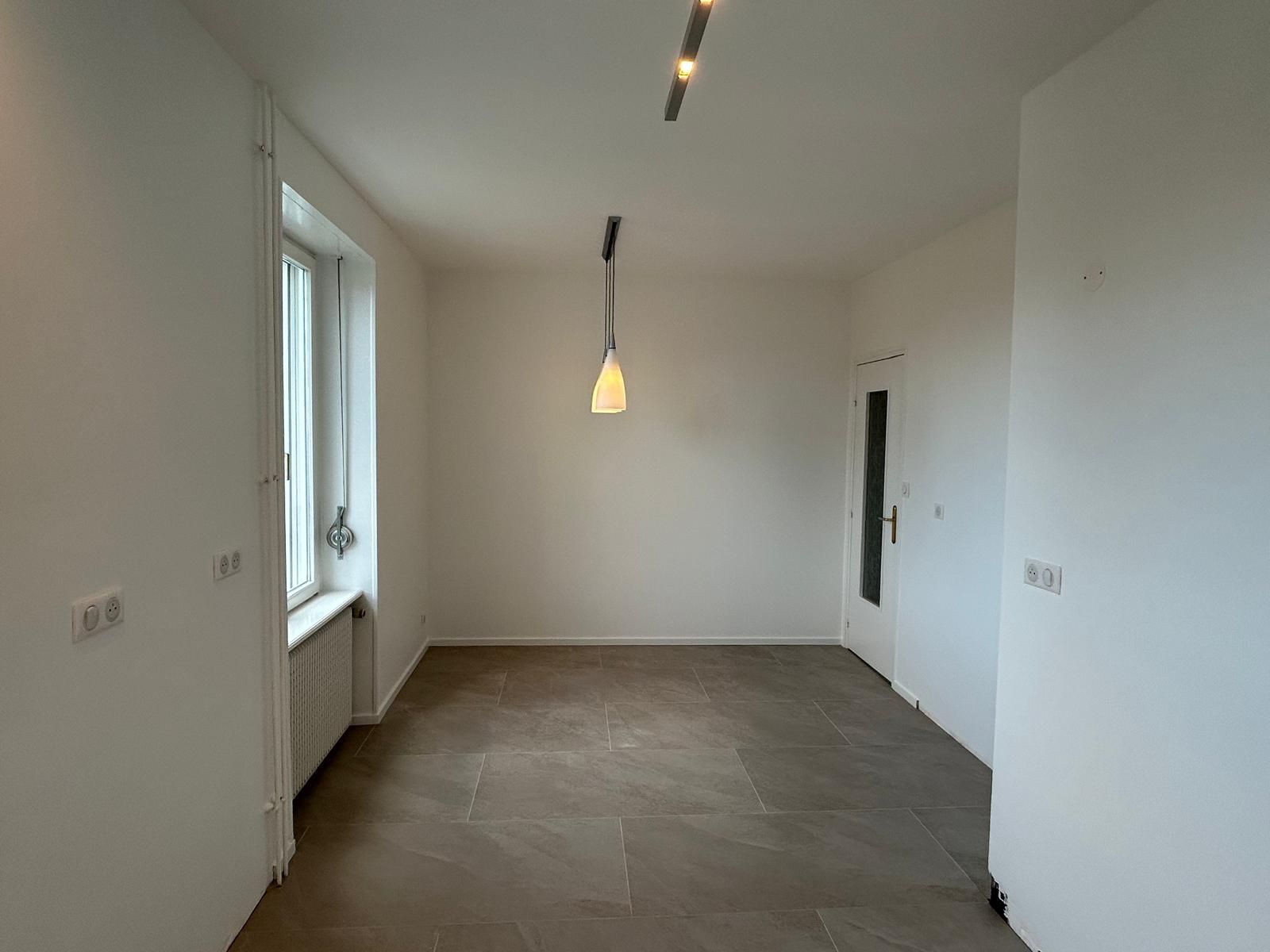 Chambre d'appartement blanche vide avec parquet, fenêtres et luminaires suspendus au plafond