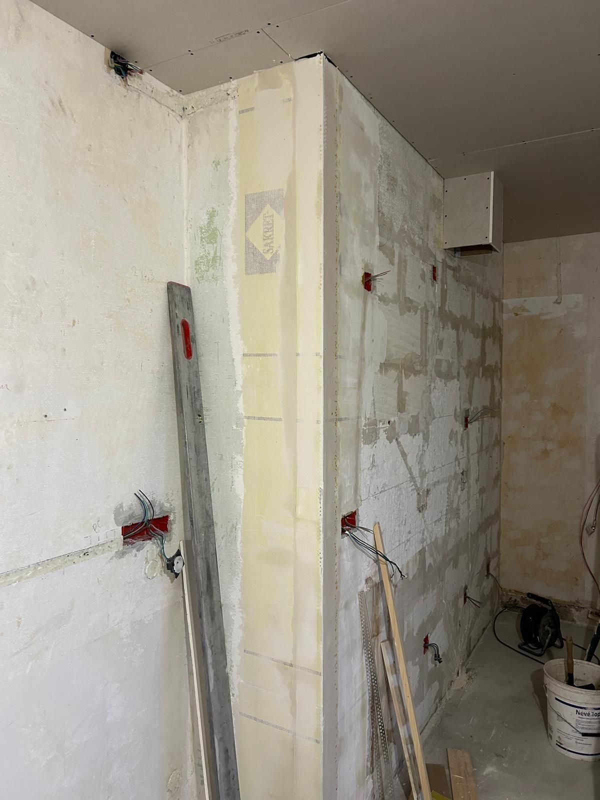 Salle de bain partiellement rénovée avec murs carrelés, plomberie apparente et outils appuyés contre le mur.