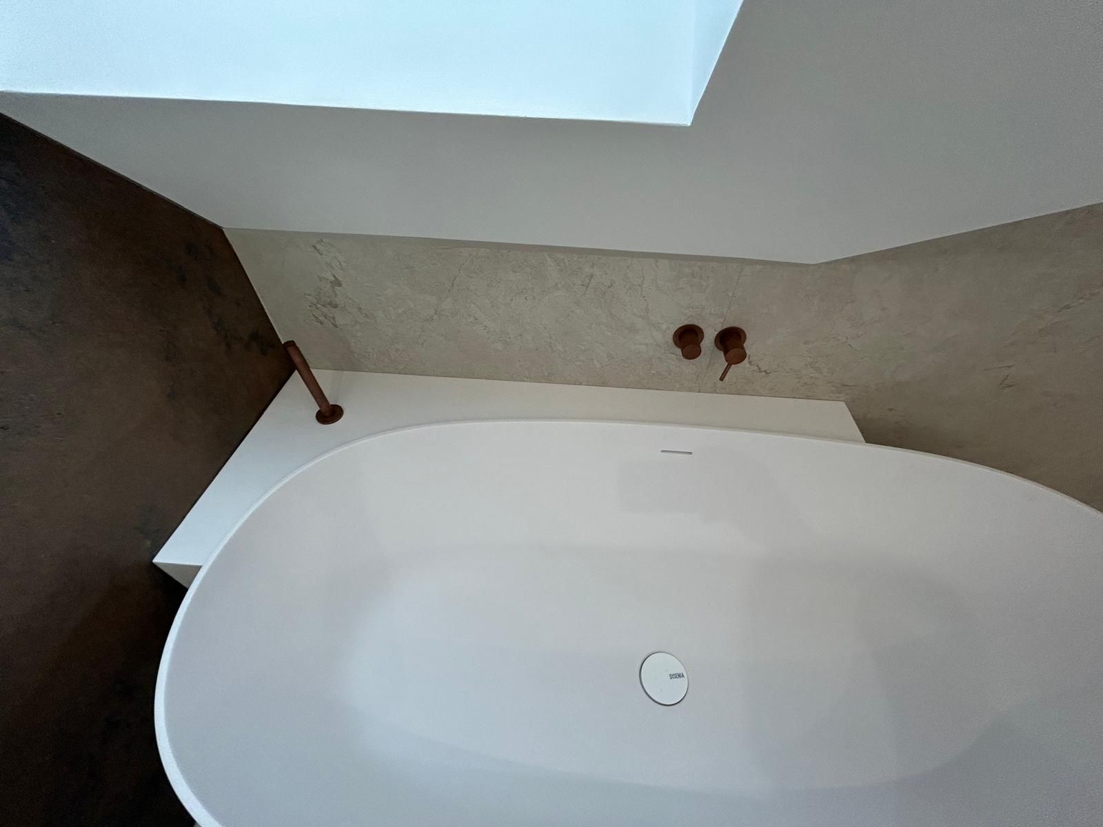 Une baignoire blanche installée dans une salle de bain minimaliste avec des accessoires en cuivre 