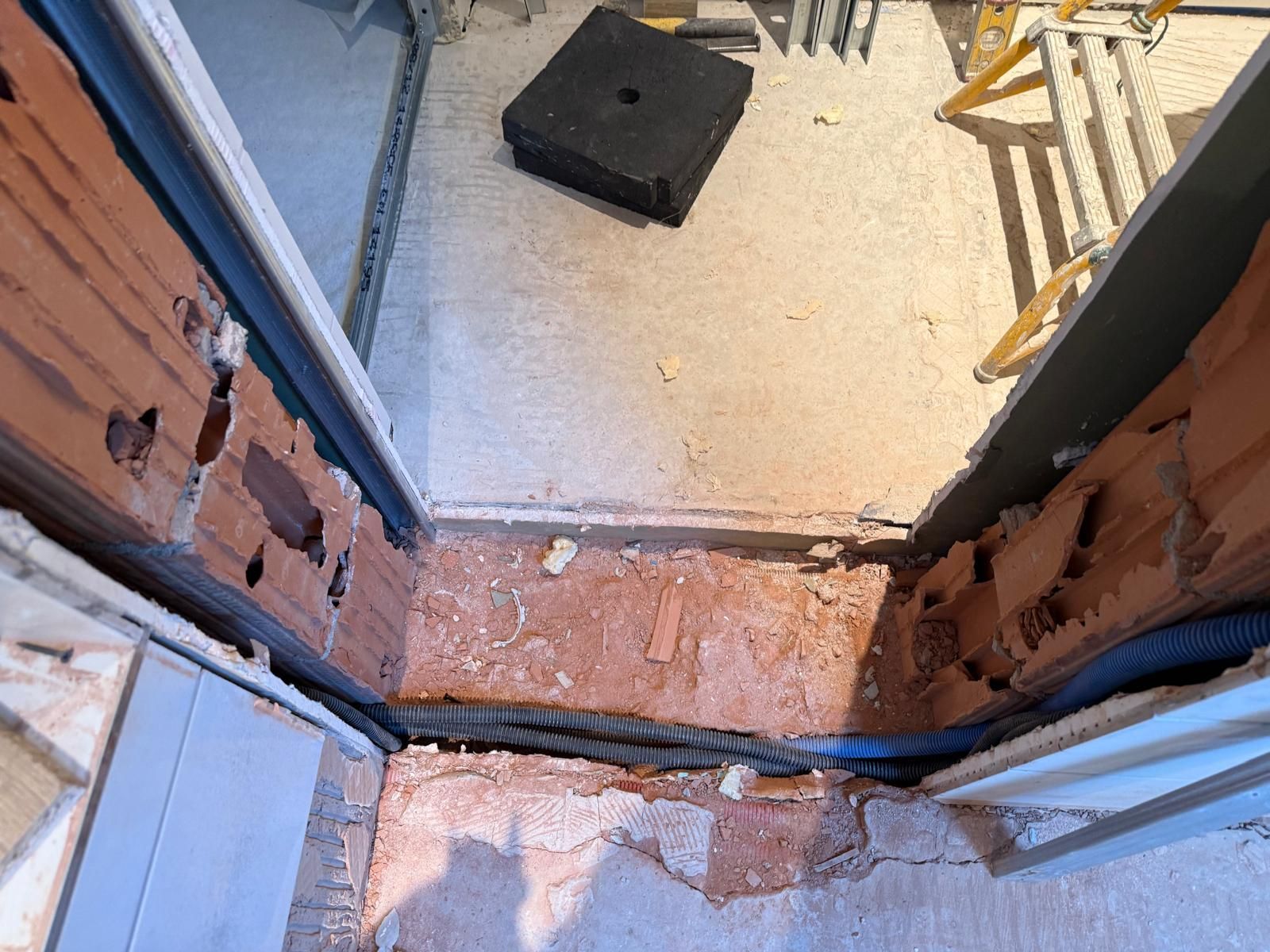 Porte endommagée avec briques apparentes et débris suite à des travaux de construction ou de rénovation.