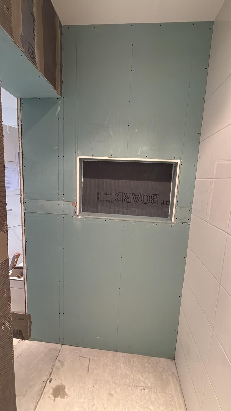 Cabine de douche carrelée en cours de construction avec une petite niche encastrée dans un mur du fond vert turquoise.