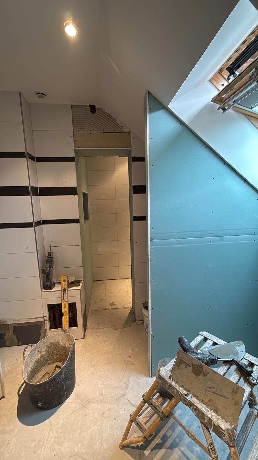 Pièce partiellement rénovée avec mur bleu, échelle, outils et porte en construction