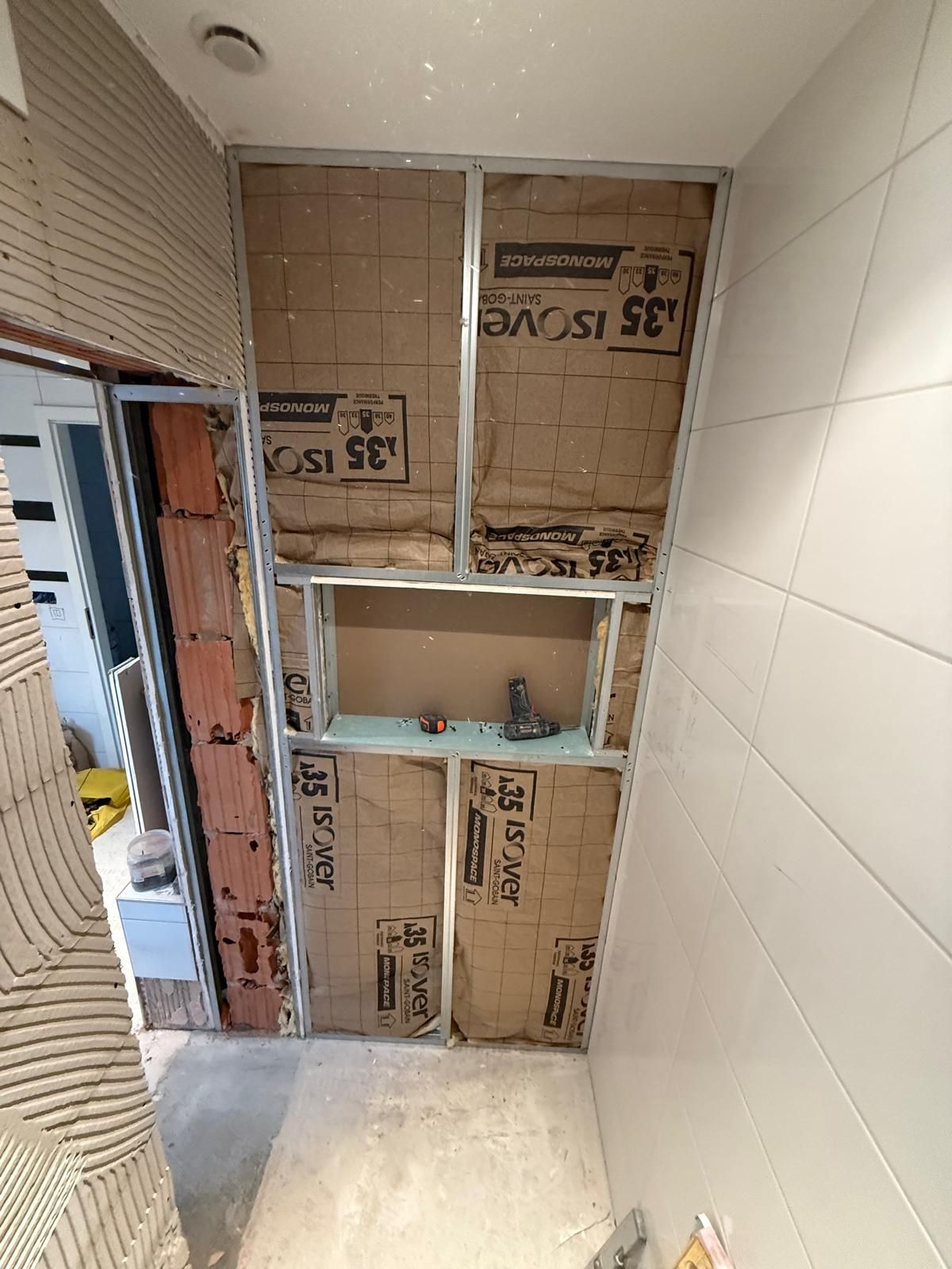 Salle de bains en rénovation avec ossature murale apparente, isolation et petite étagère intégrée.