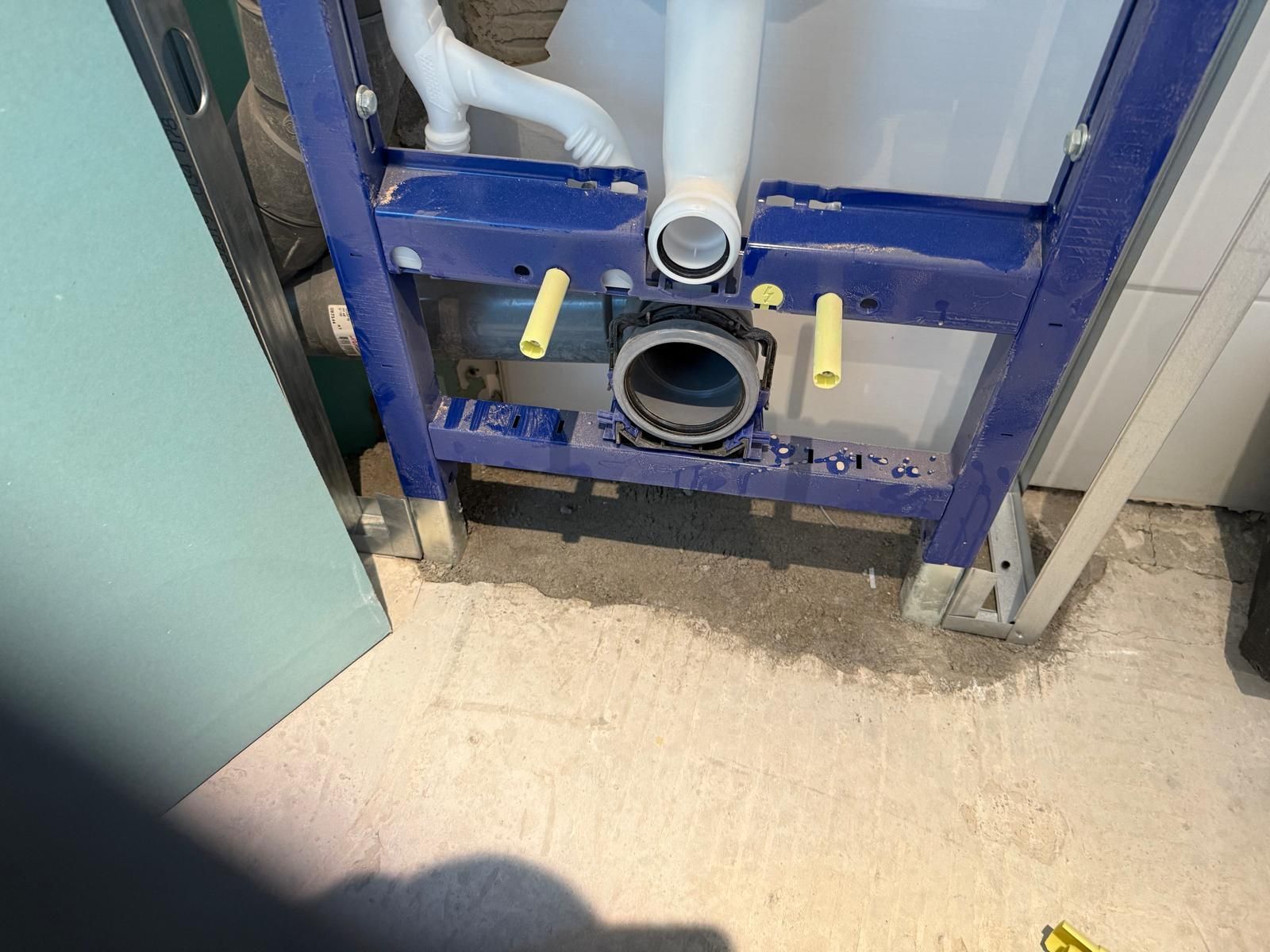 Cadre de toilettes suspendu bleu avec tuyauterie et orifice d'évacuation apparents dans une salle de bains en construction