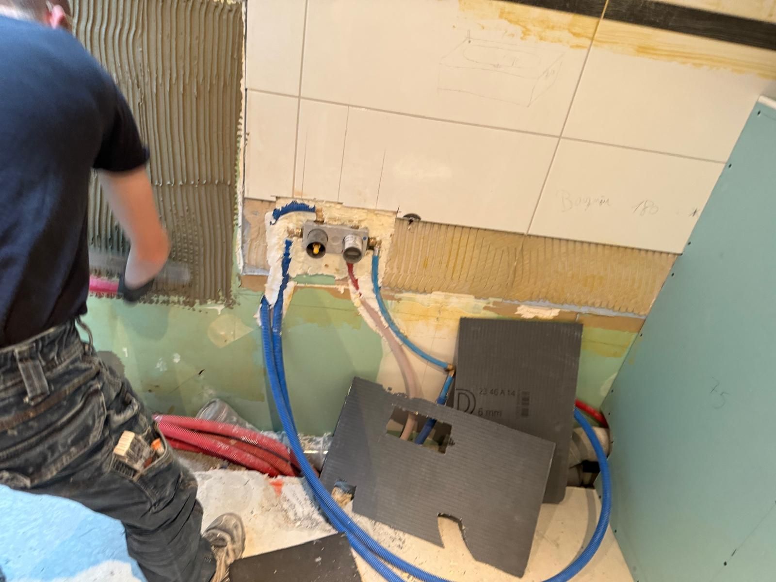 Plombier installant des tuyaux bleus et rouges le long d'un mur carrelé dans une zone de rénovation