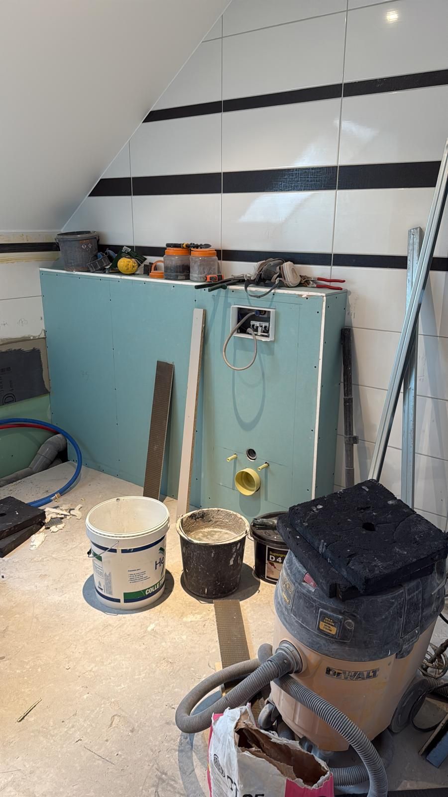 Atelier avec pots de peinture, seaux et aspirateur à côté d'une armoire turquoise contre un mur carrelé.