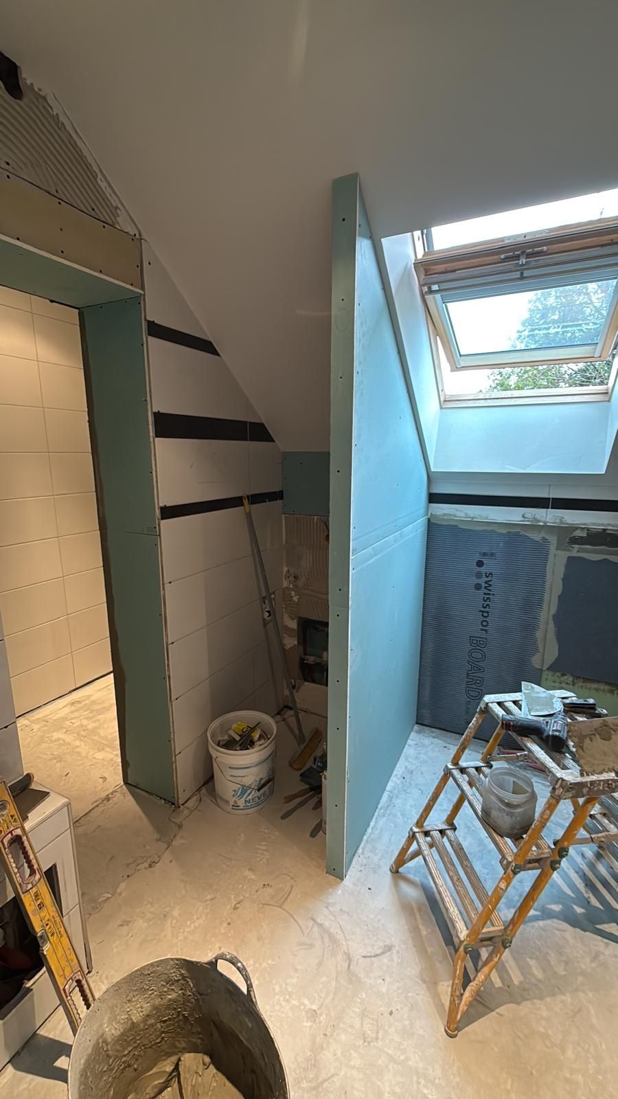 Escalier étroit en rénovation, recouvert de bâches de protection bleues, outils et puits de lumière au plafond