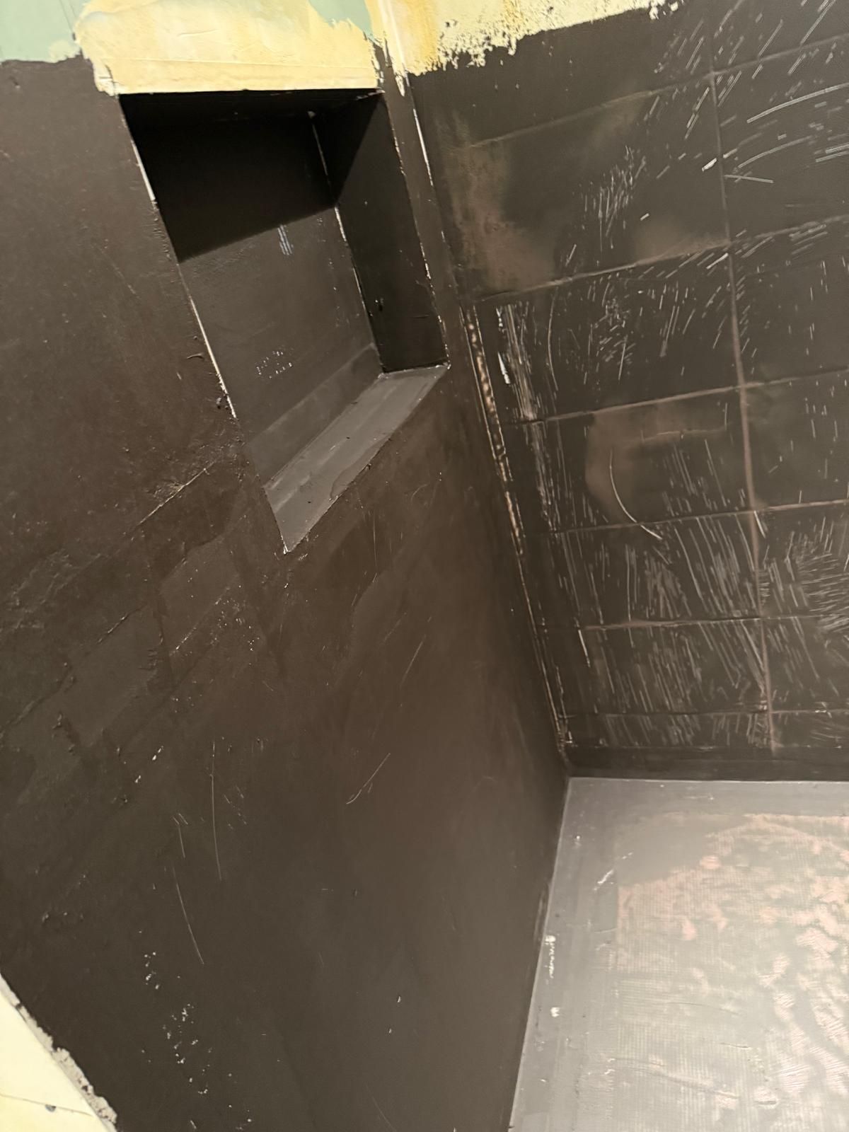 Coin intérieur aux murs noirs, avec une petite ouverture rectangulaire près du plafond et un sol usé.