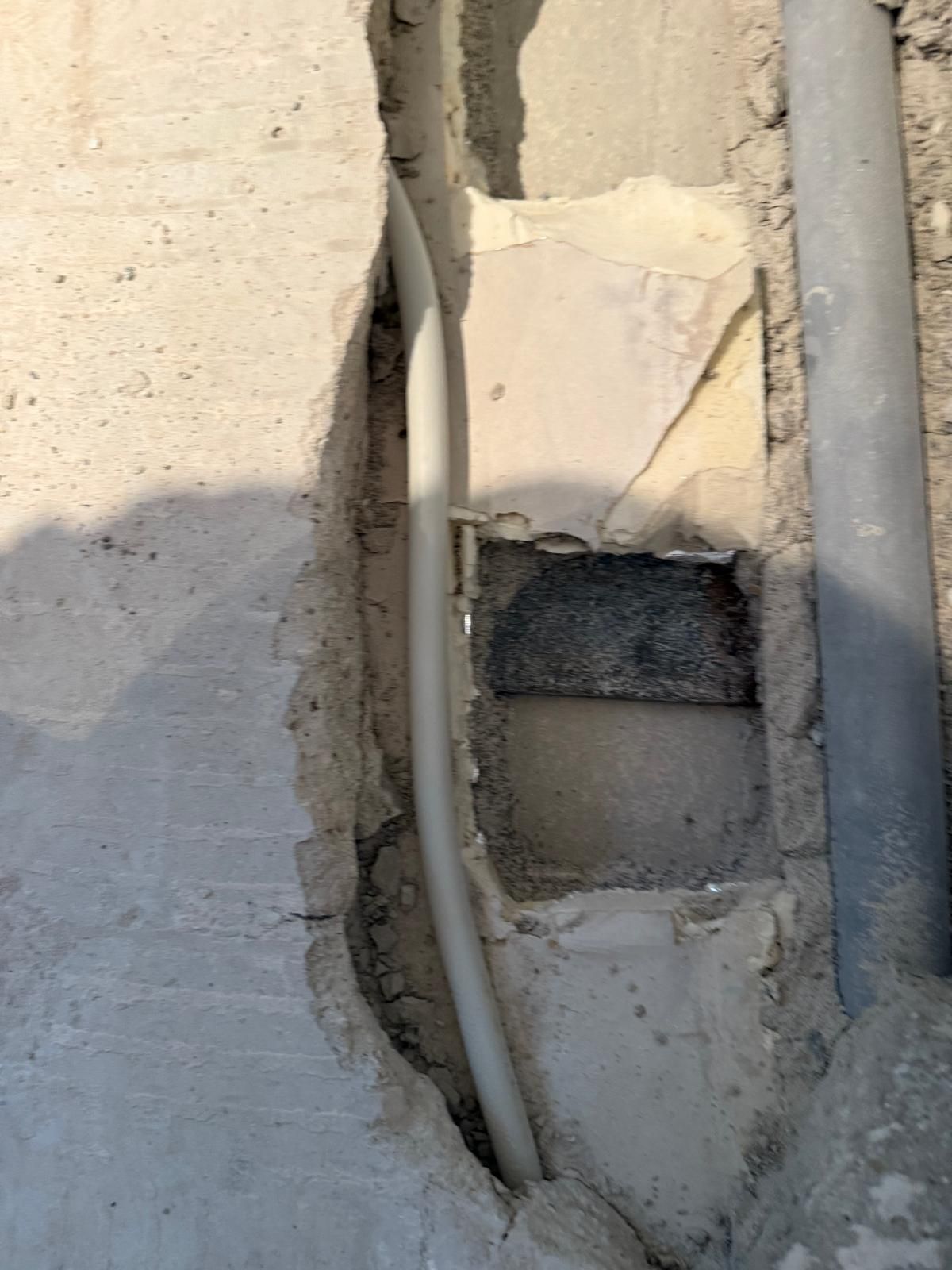Gros plan sur un mur fissuré laissant apparaître des câbles électriques et une réparation de fortune.