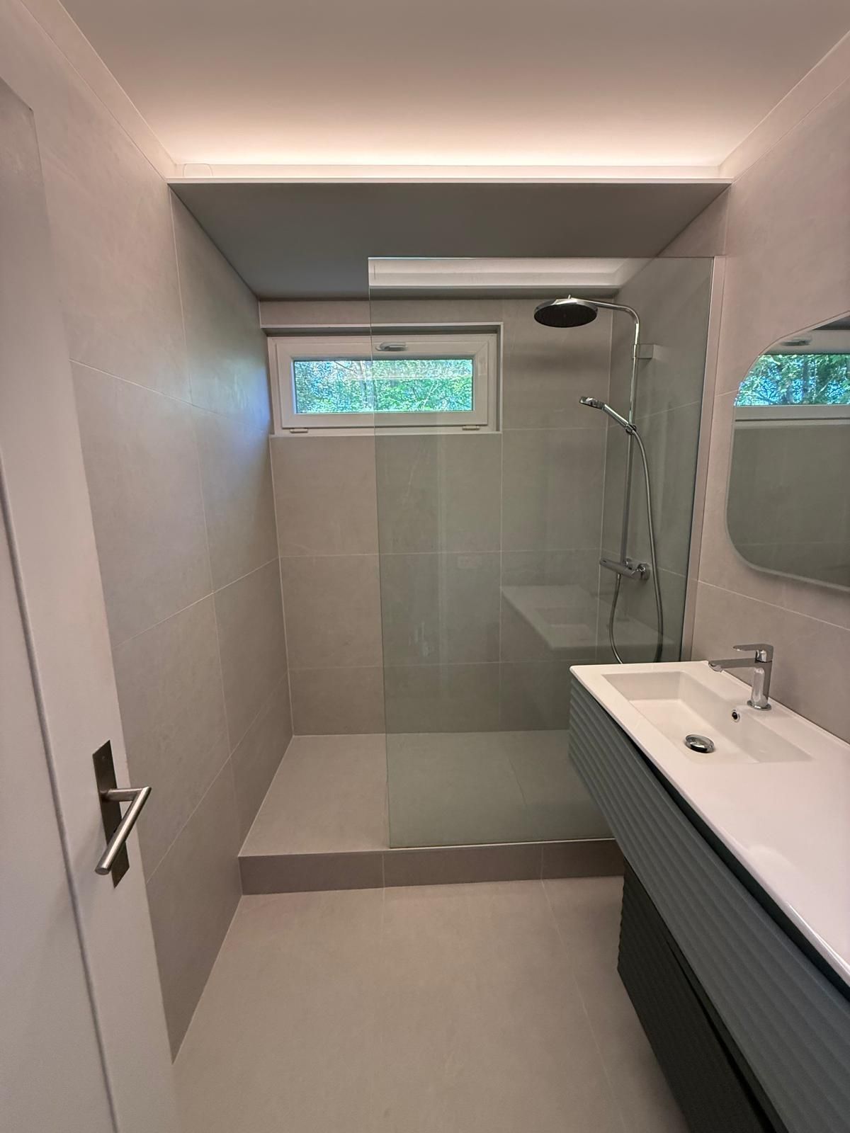 Salle de bain moderne et minimaliste avec douche en verre, meuble-lavabo blanc et petite fenêtre