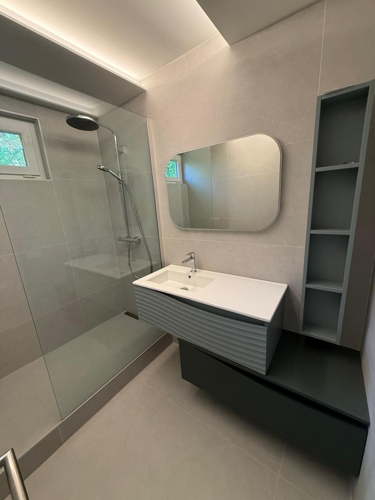 Salle de bains moderne avec douche en verre, lavabo mural, miroir et étagères grises