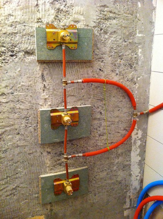 Un tas de tuyaux sont accrochés au mur d'une salle de bain.