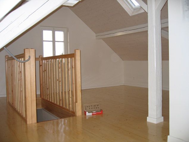 Chambre mansardée avec parquet et garde-corps. Murs blancs, plafond mansardé.