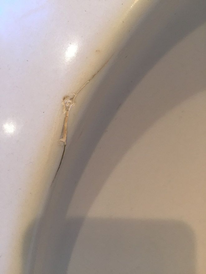 Gros plan d'une surface en céramique blanche fissurée, avec une petite formation en forme de bulle.