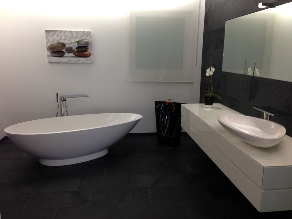 Salle de bain moderne avec baignoire ovale blanche, lavabo blanc et sol noir.
